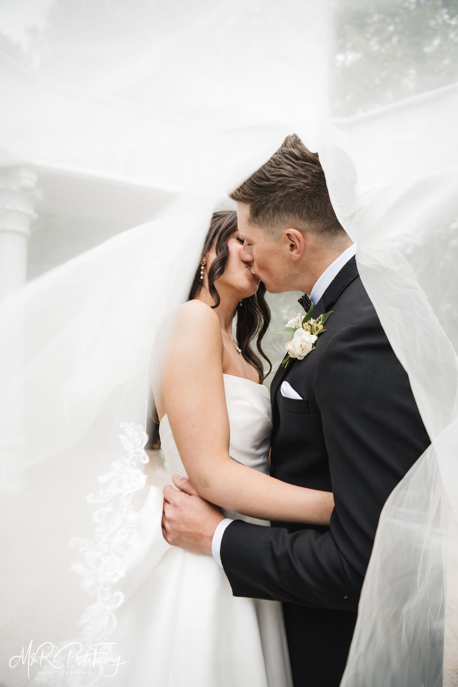 Bride and groom share a passionate kiss enveloped by a flowing lace-trimmed veil.