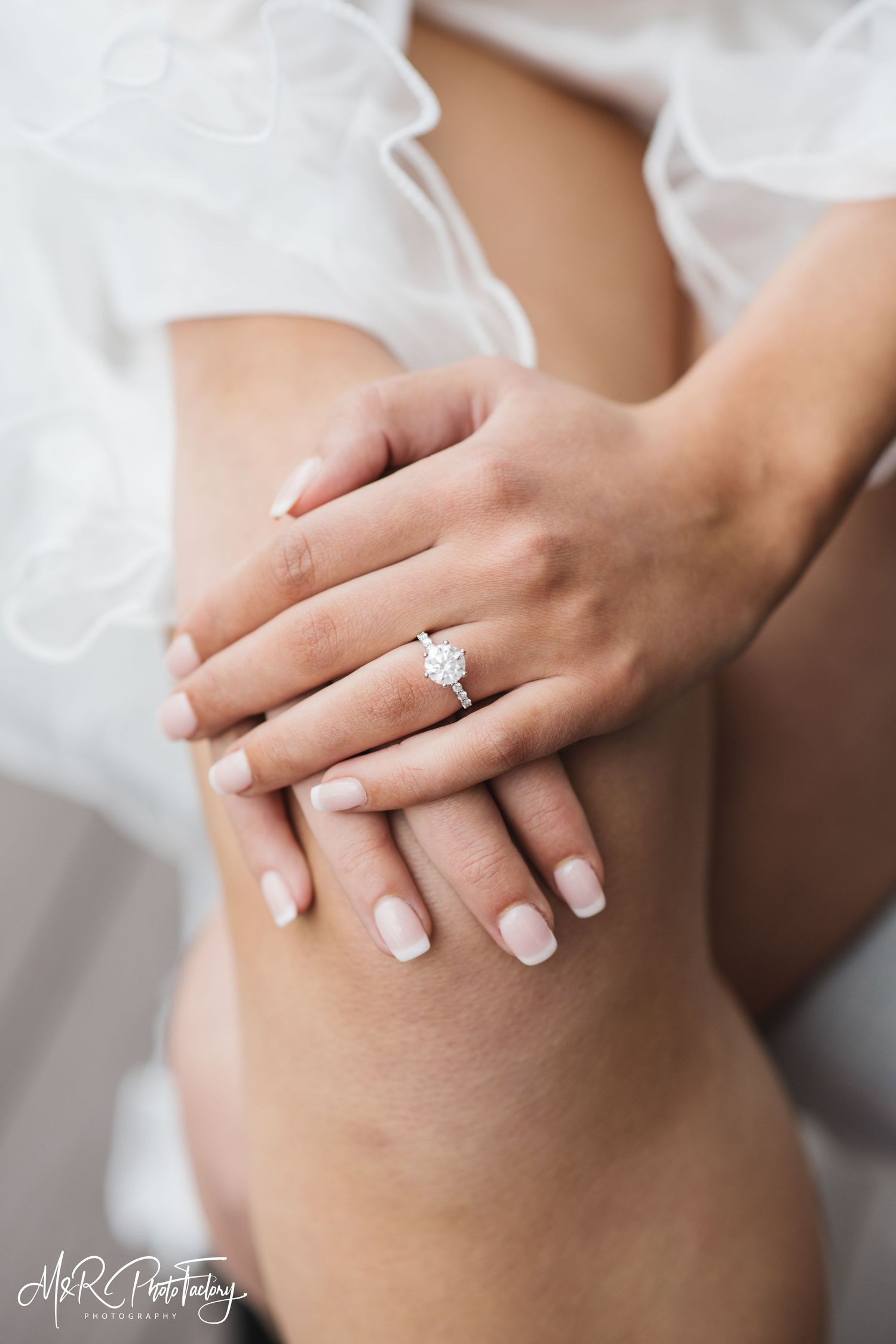 Close-up of a bride\u2019s hands resting on her knee showcasing a stunning solitaire engagement ring.