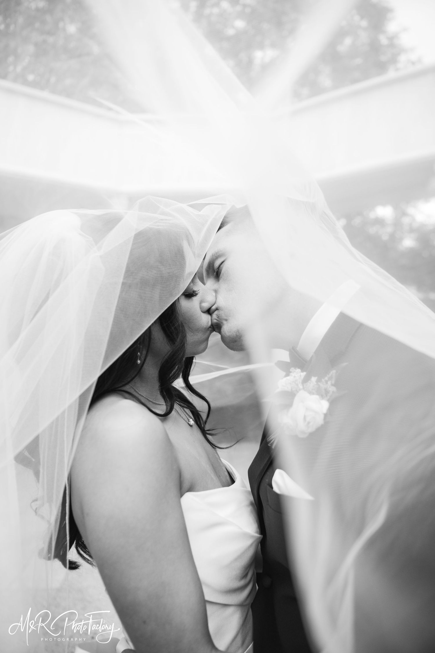 Black and white photo of newlyweds kissing under a billowing wedding veil.