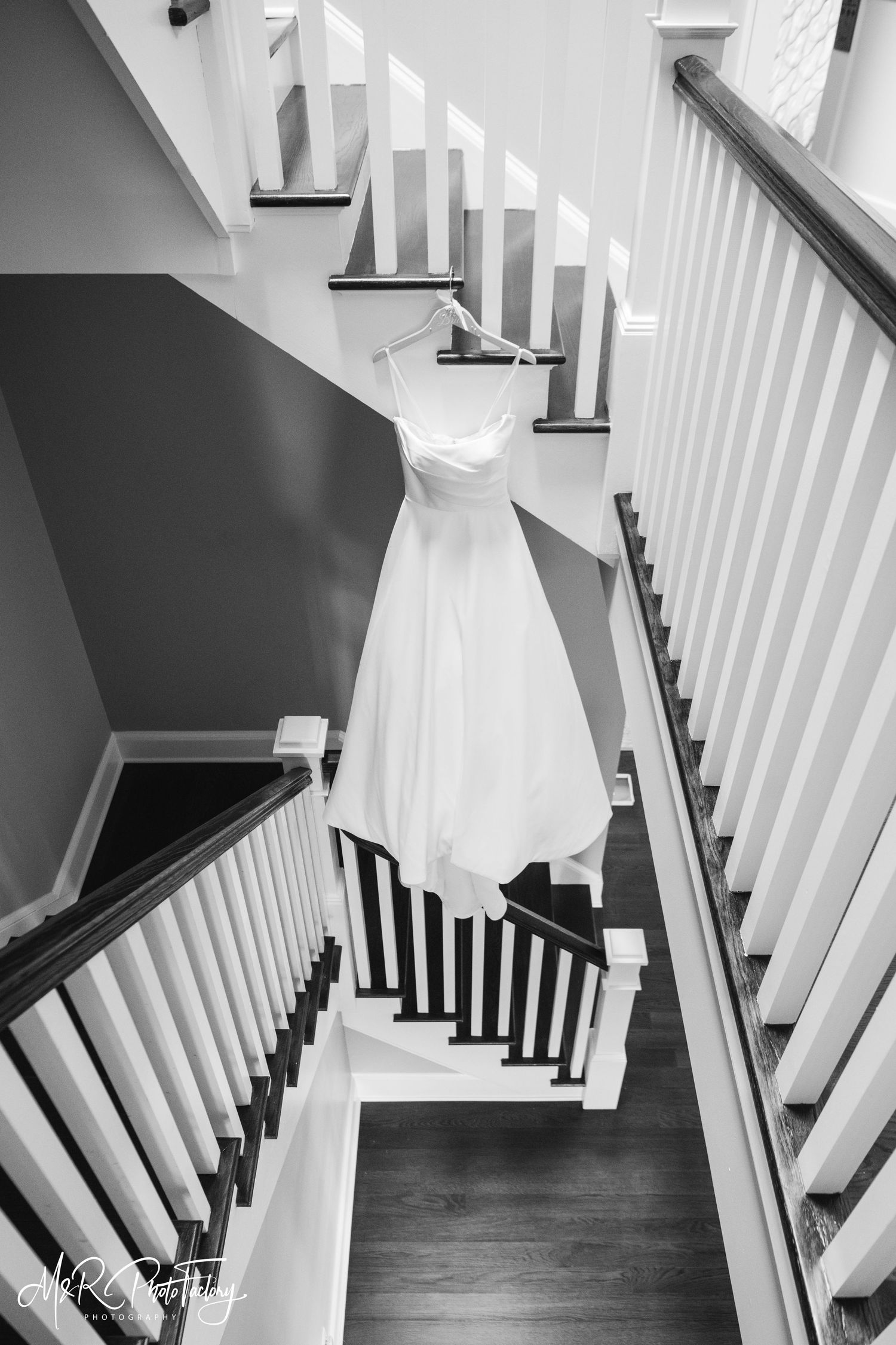 Elegant white wedding gown hanging on a staircase railing in a black and white photo.