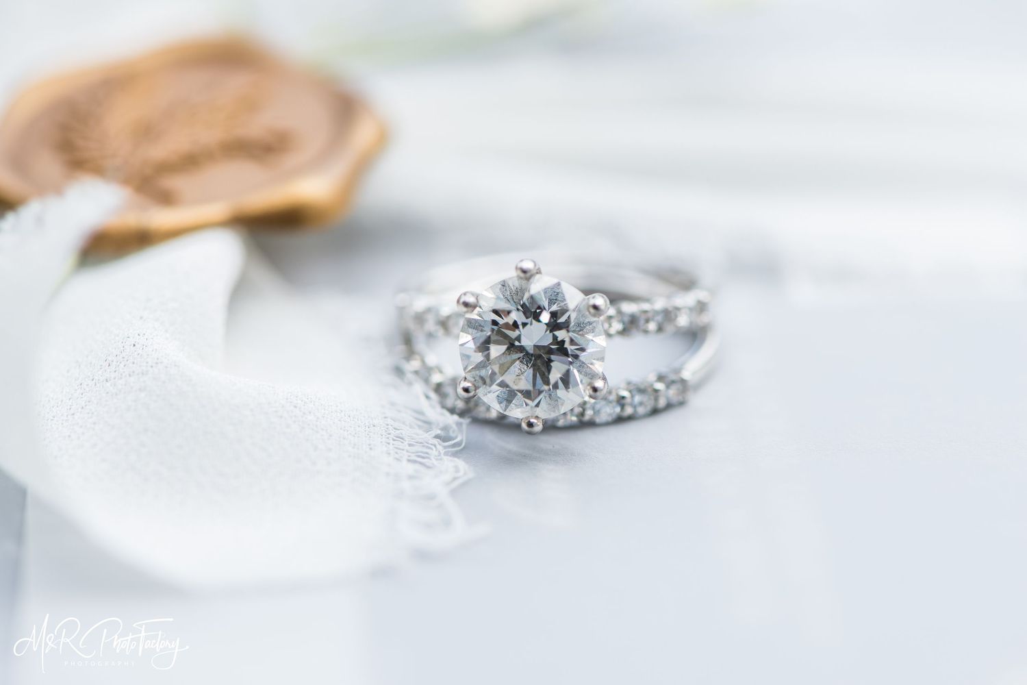 Close-up of a stunning round diamond engagement ring with diamond wedding band on white fabric.