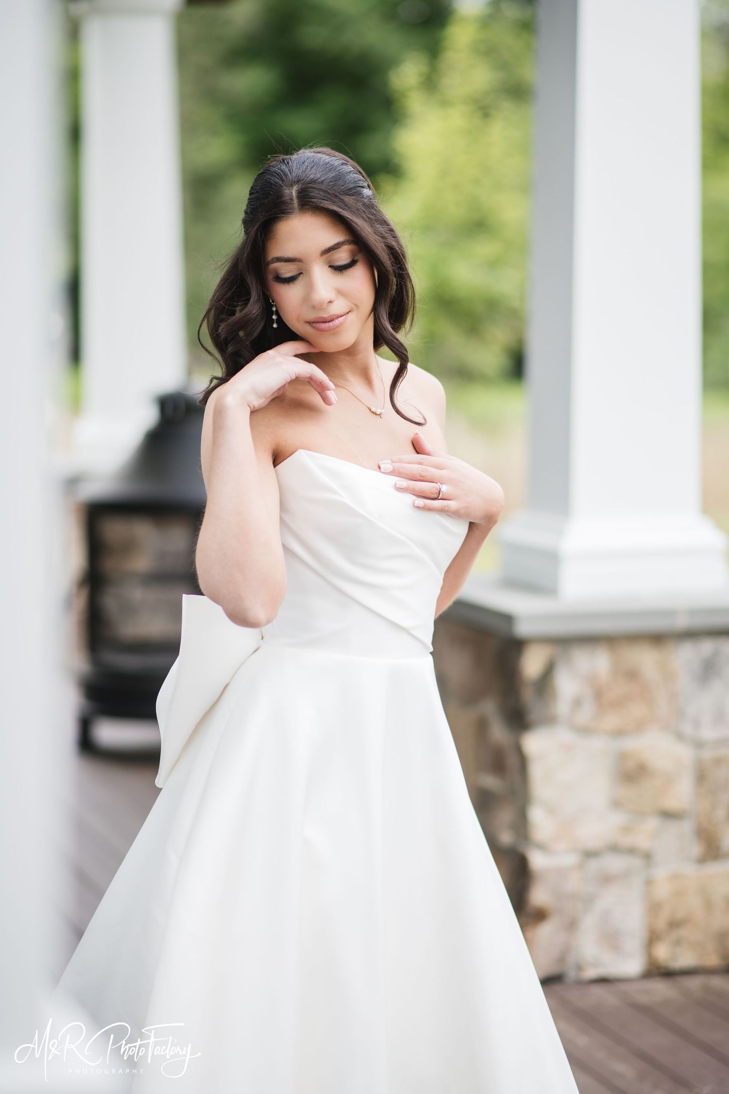 Close-up of a bride in a strapless white gown with bow detail posing near white columns.