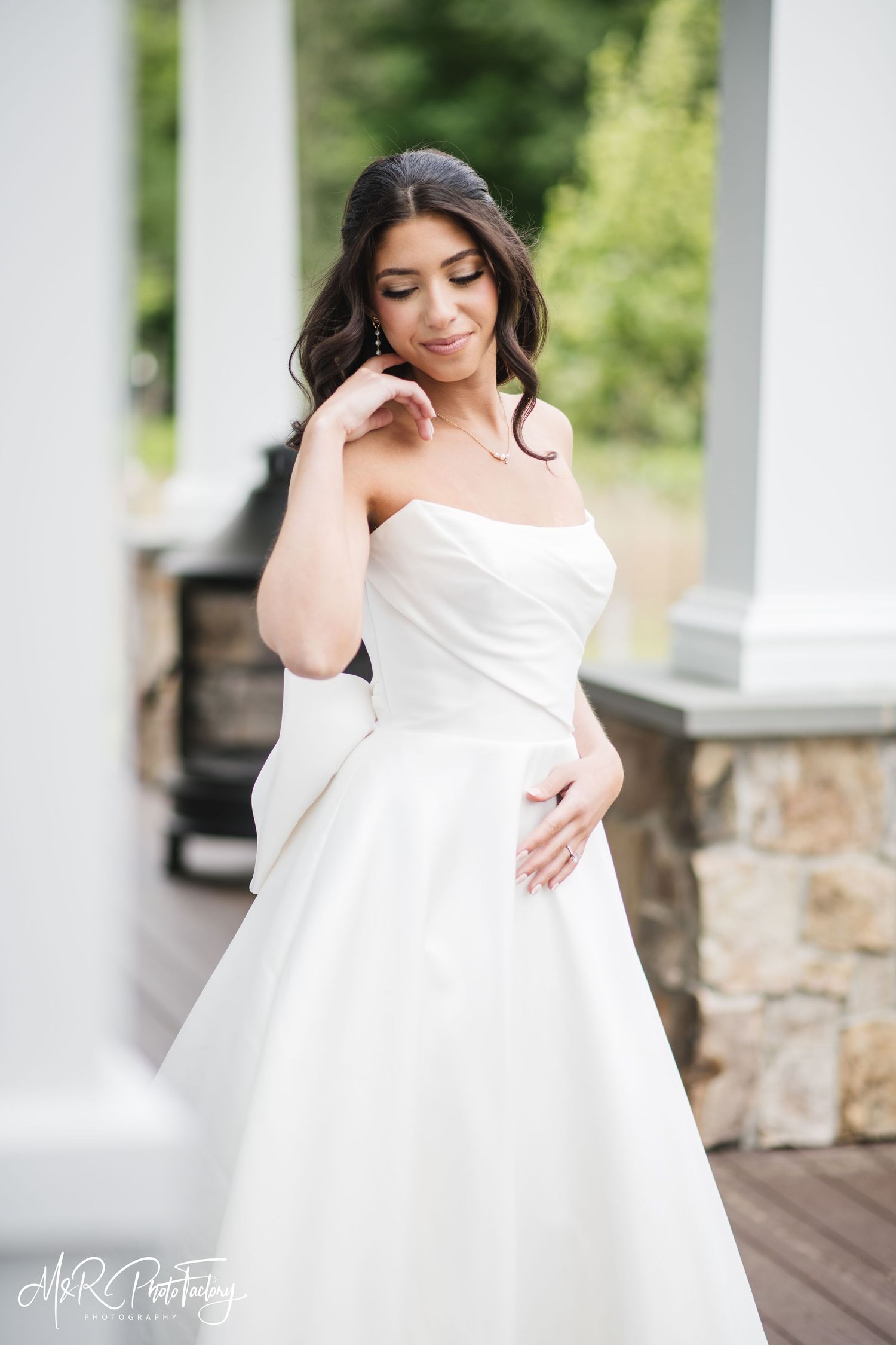 Elegant bride in a strapless white wedding dress with bow posing near white columns outdoors.