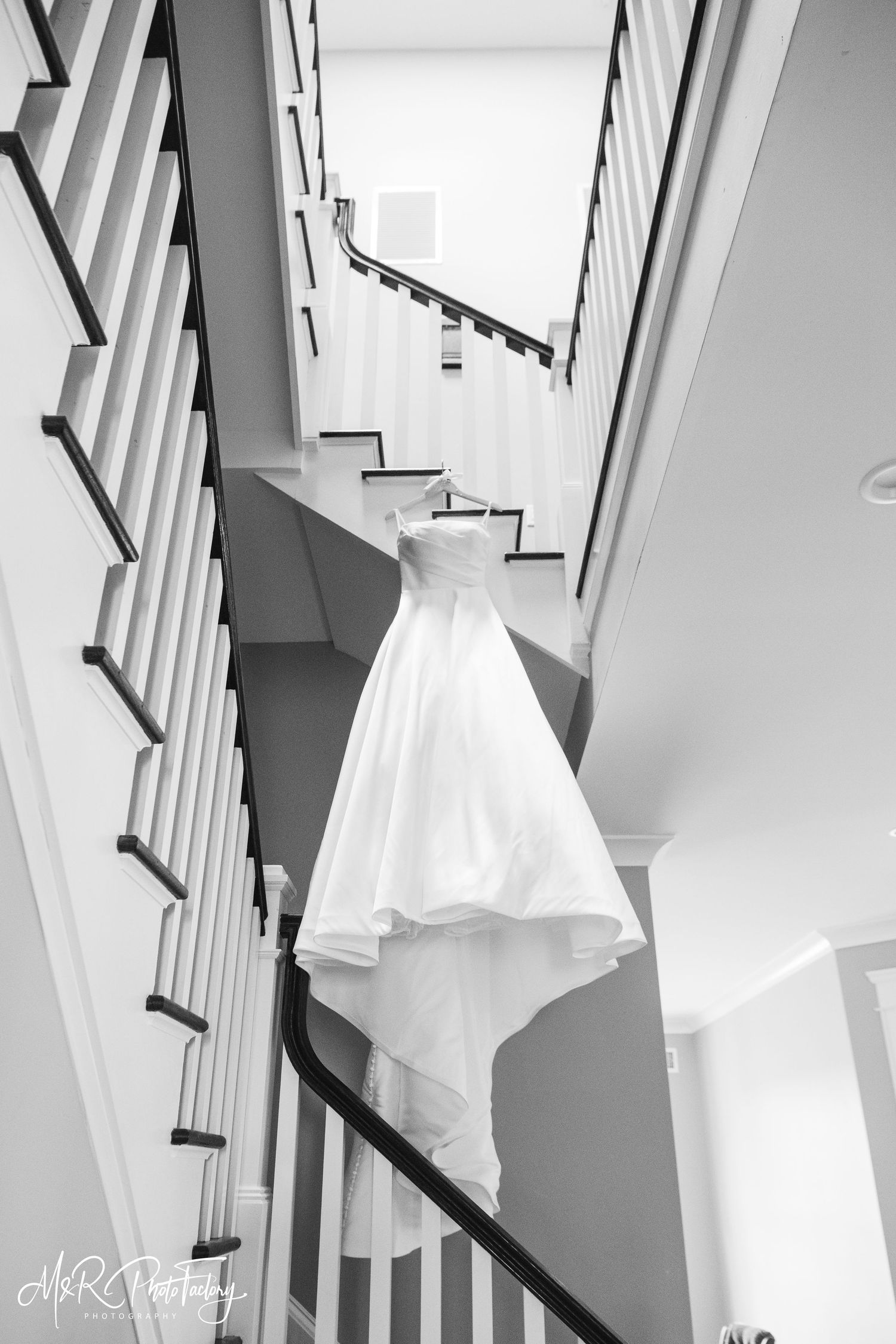 Black and white photo of a elegant ball gown wedding dress hanging on a curved staircase railing.