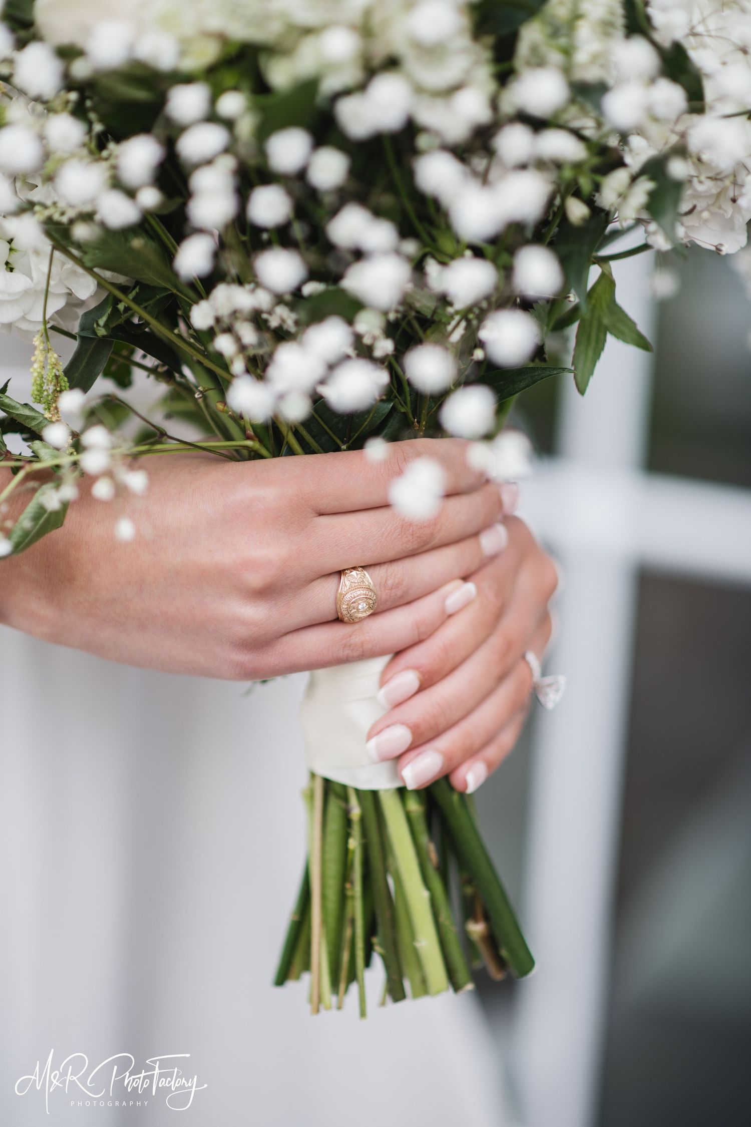 Bride's hands with French manicure holding white baby's breath bouquet with gold signet ring detail.