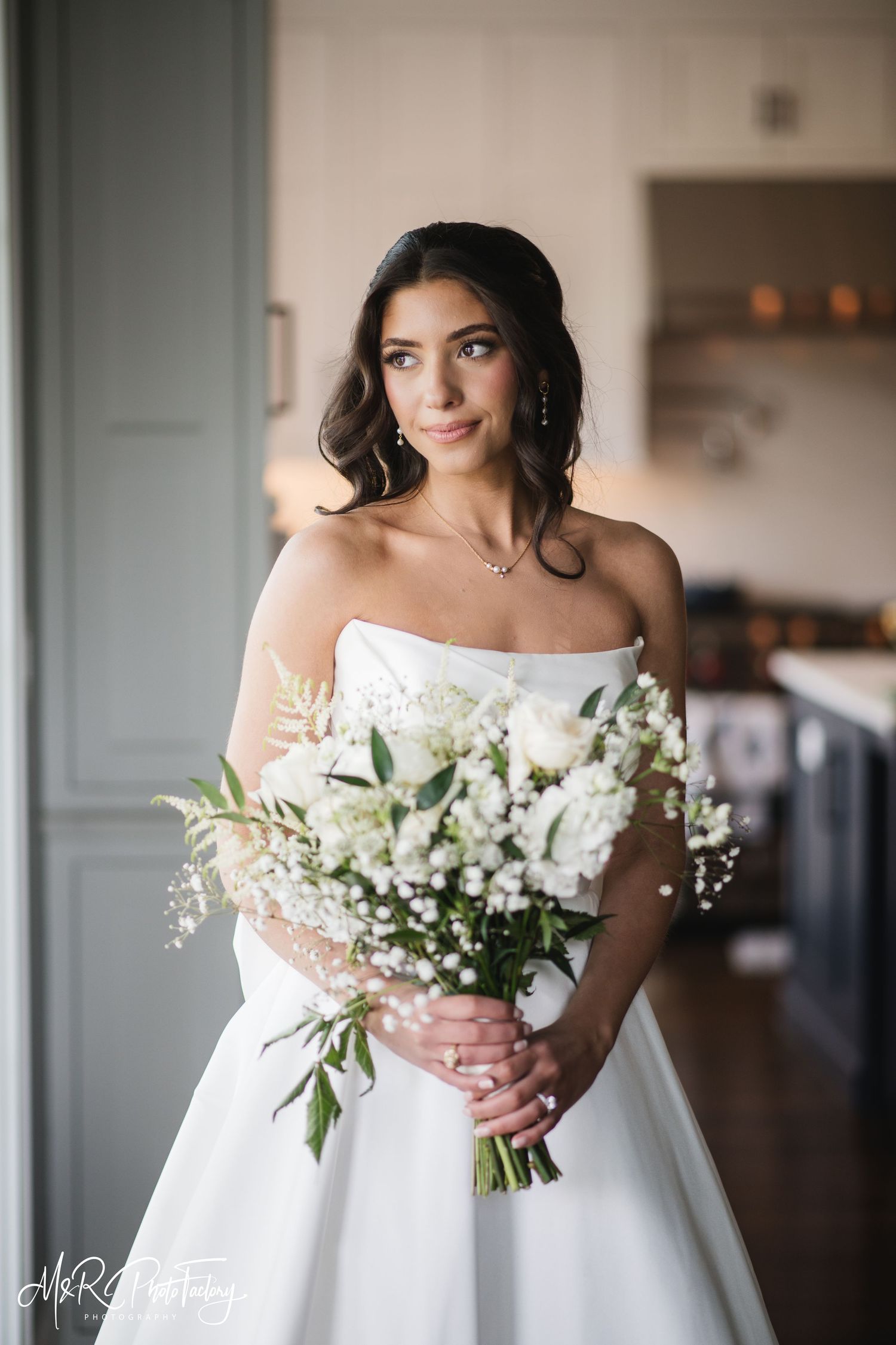 Bride in strapless white ball gown holding white rose and baby's breath bouquet with a serene expression.