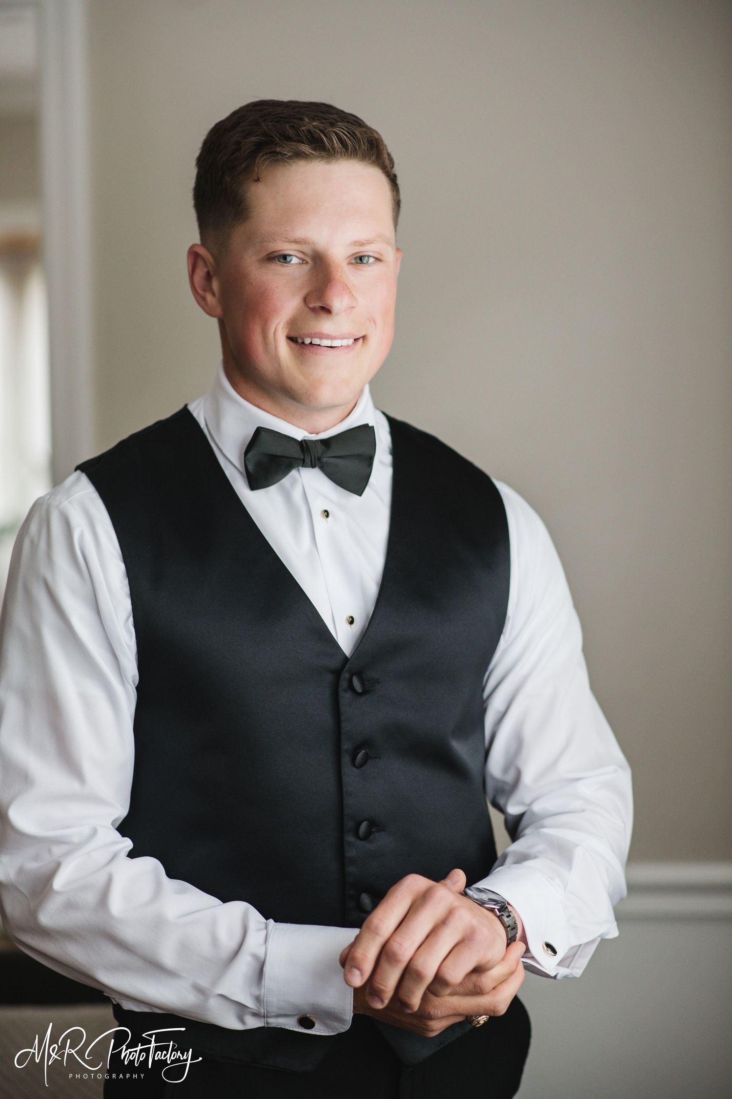 Smiling groom in black tuxedo vest and bow tie posing for wedding portrait.
