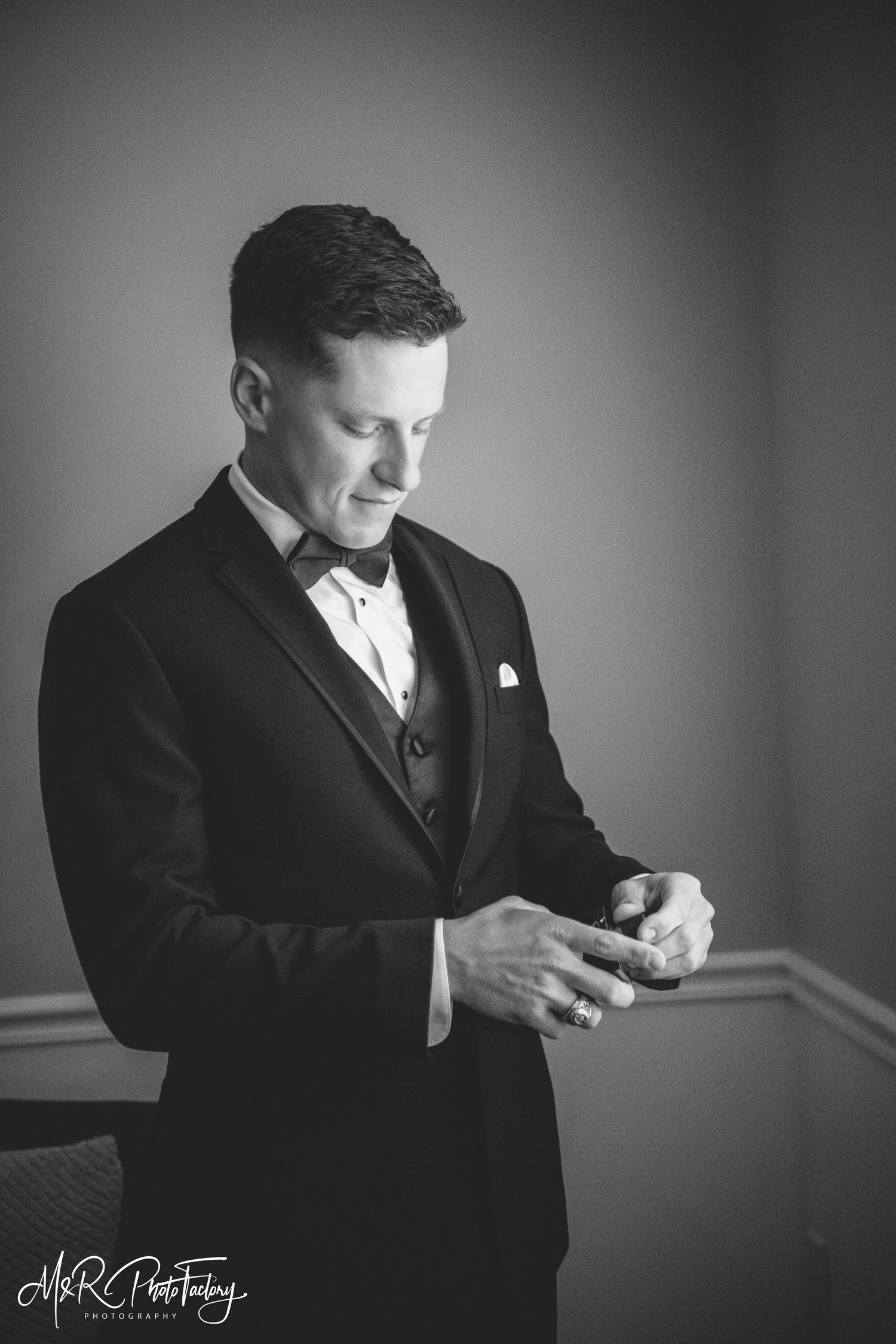 Black and white portrait of groom in tuxedo adjusting his wedding ring.