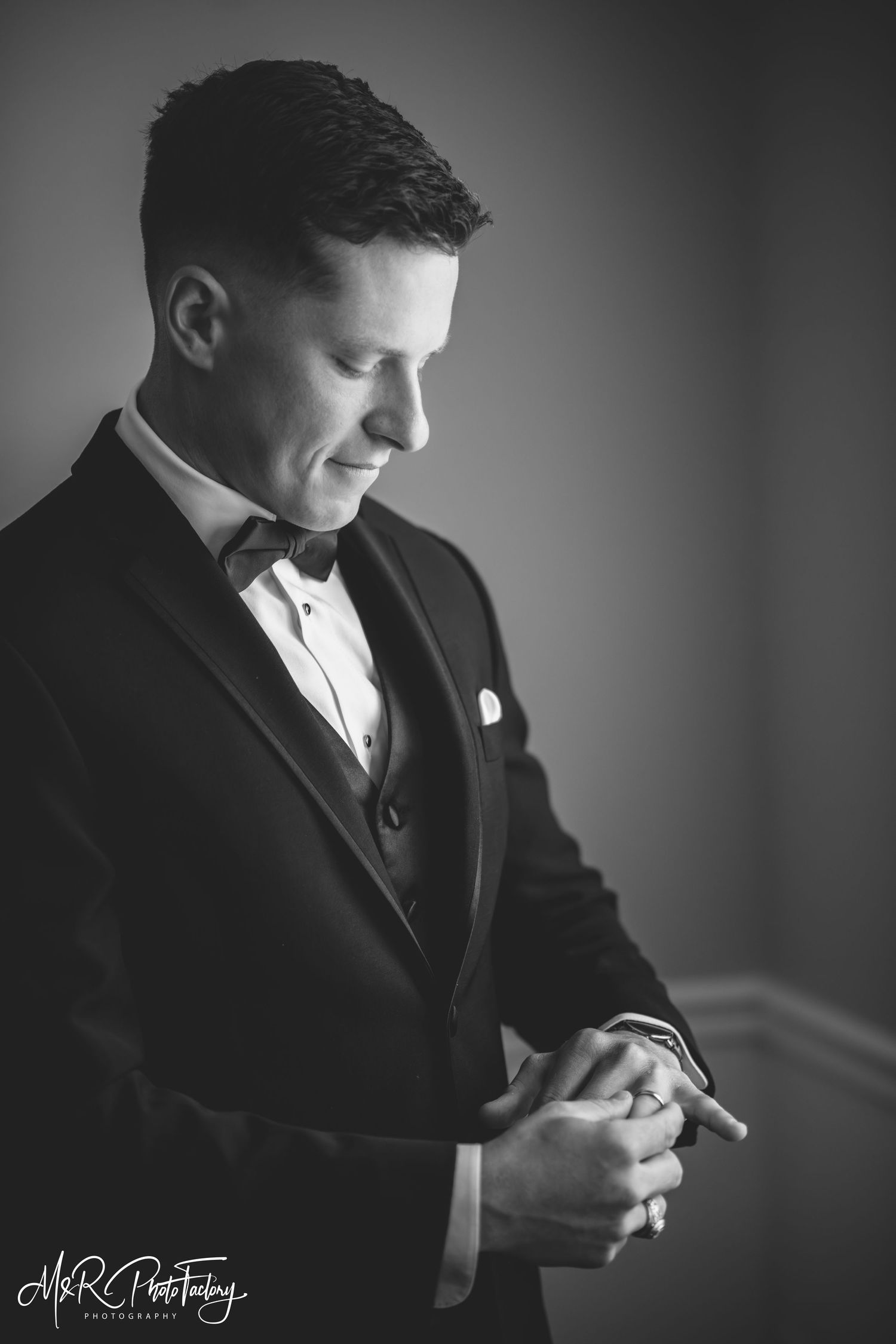 Groom in black tuxedo looks down reflectively in elegant black and white wedding photo.