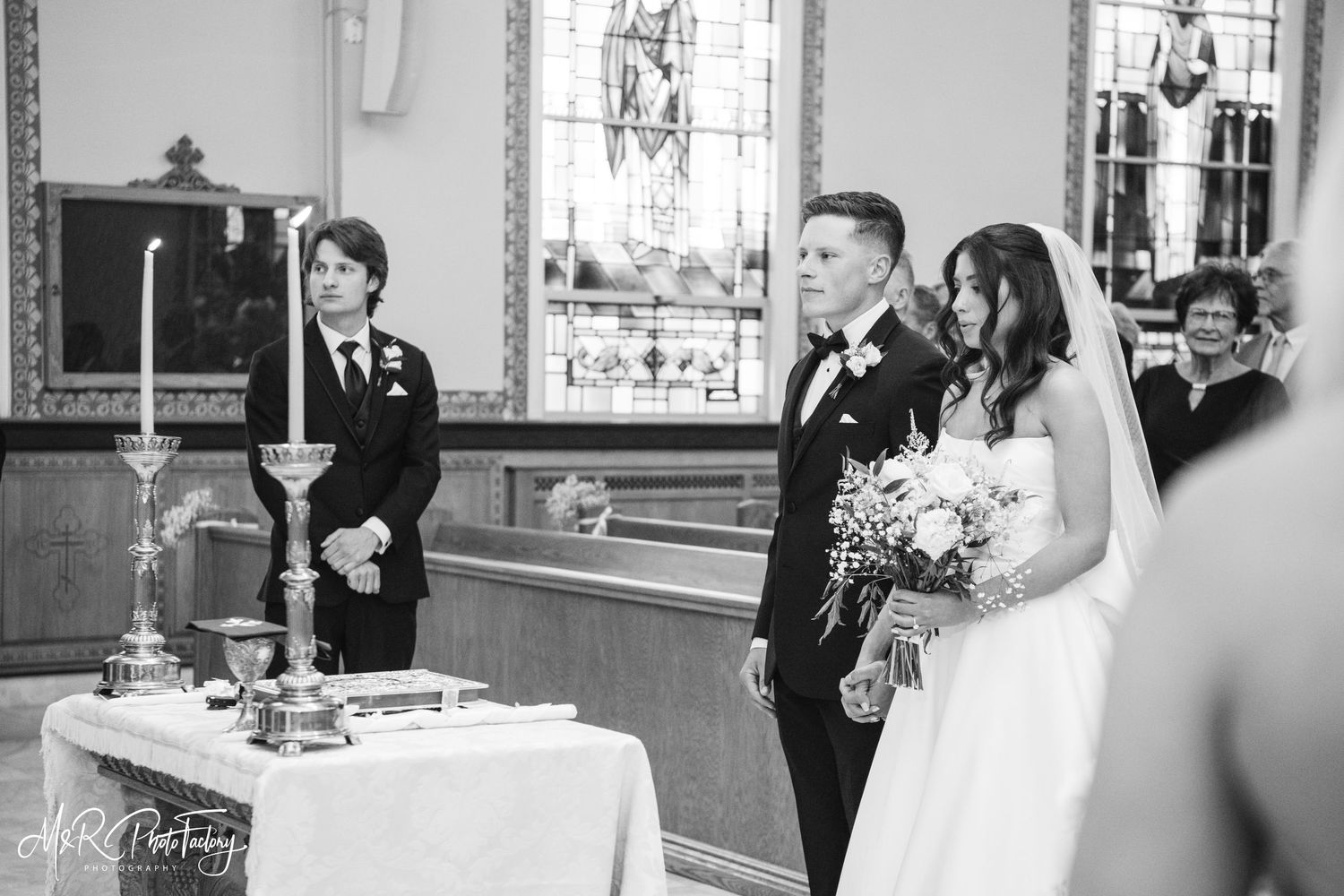 Bride and groom stand at church altar during wedding ceremony in black and white photo.