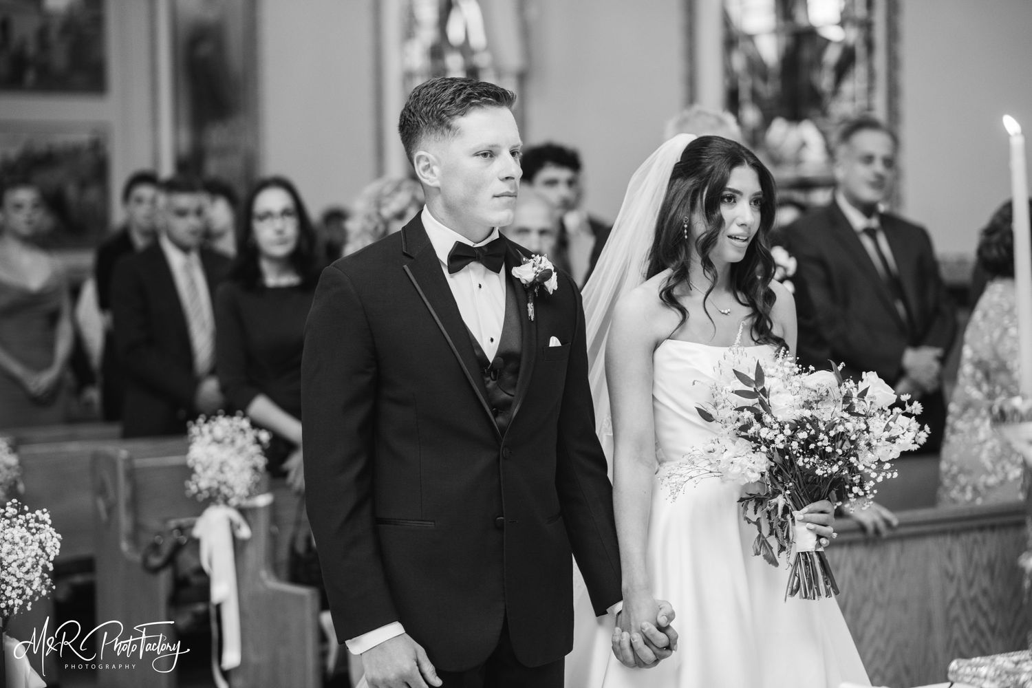 Bride and groom hold hands walking down church aisle in elegant black and white photo.