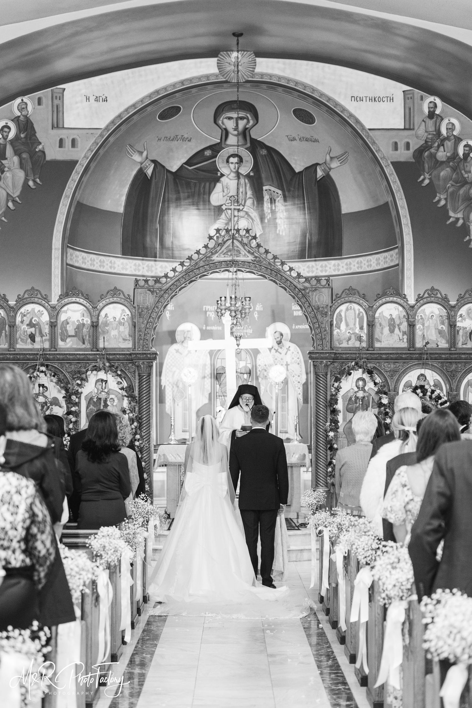 Bride and groom walk down ornate Orthodox church aisle in stunning black and white photo.