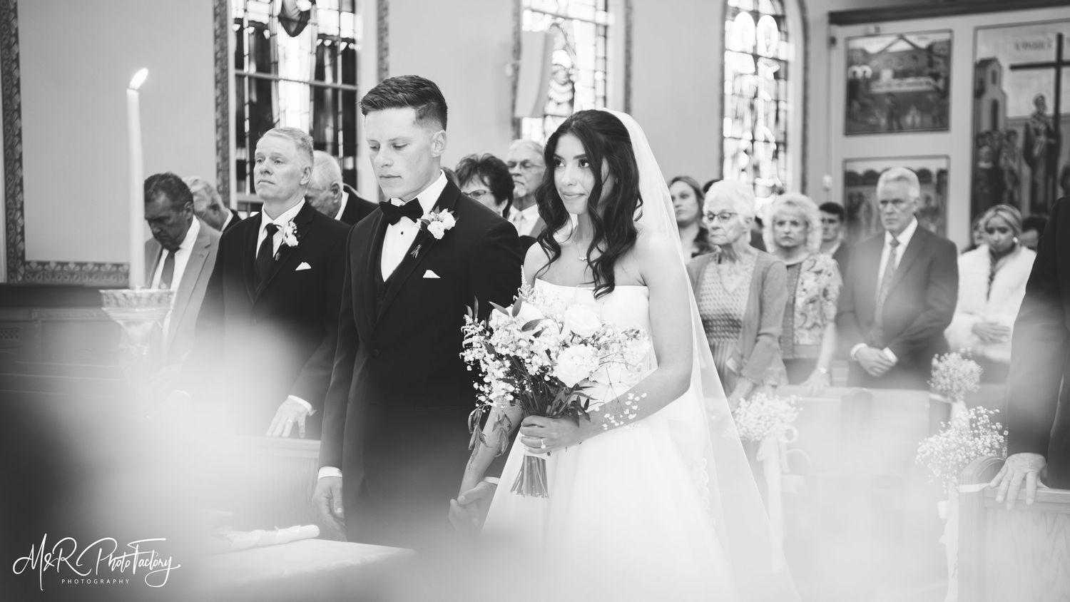 Bride with bouquet and groom stand at church altar in soft black and white portrait.