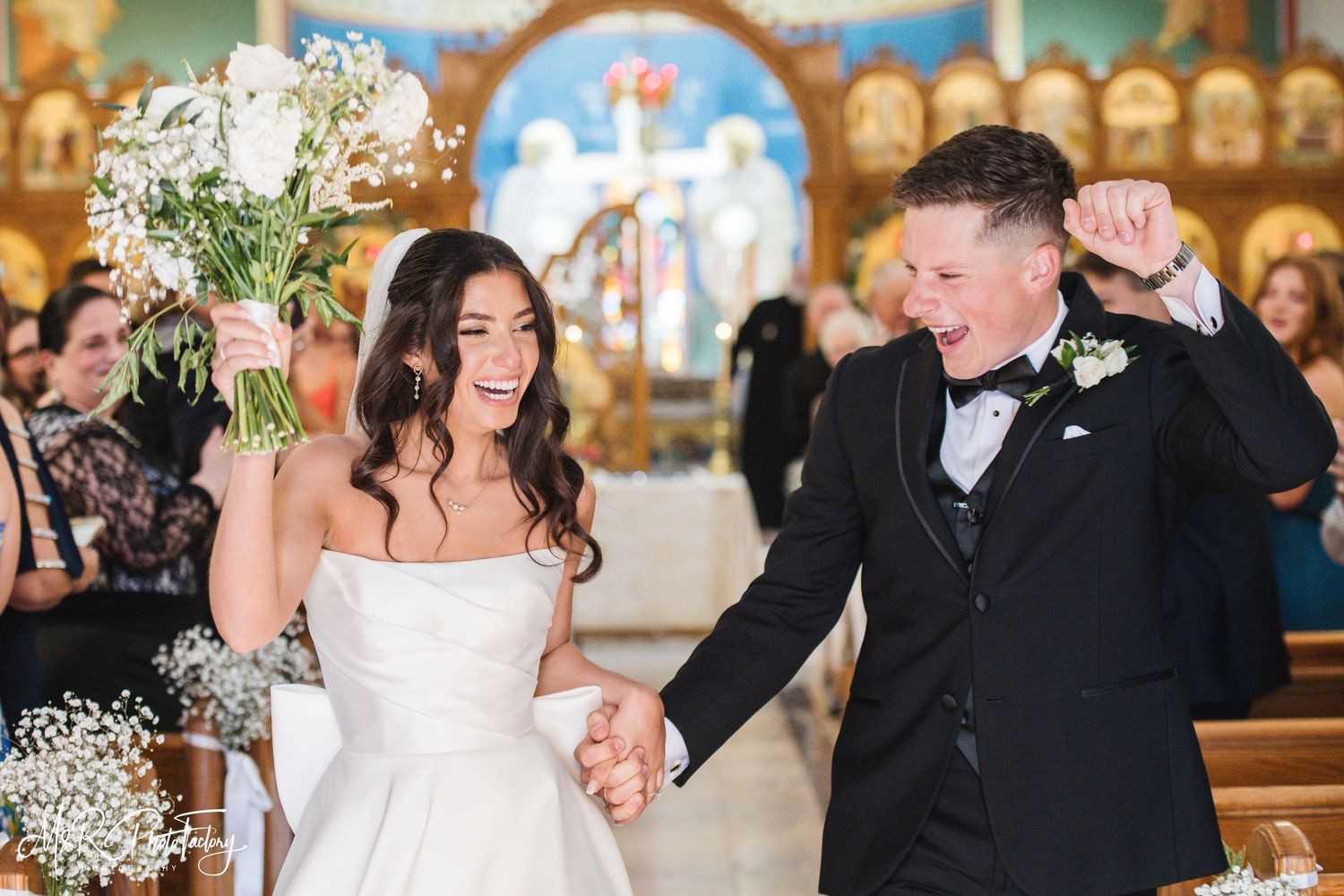 Joyful bride and groom celebrating recessional in church, bride raising bouquet, groom pumping fist.