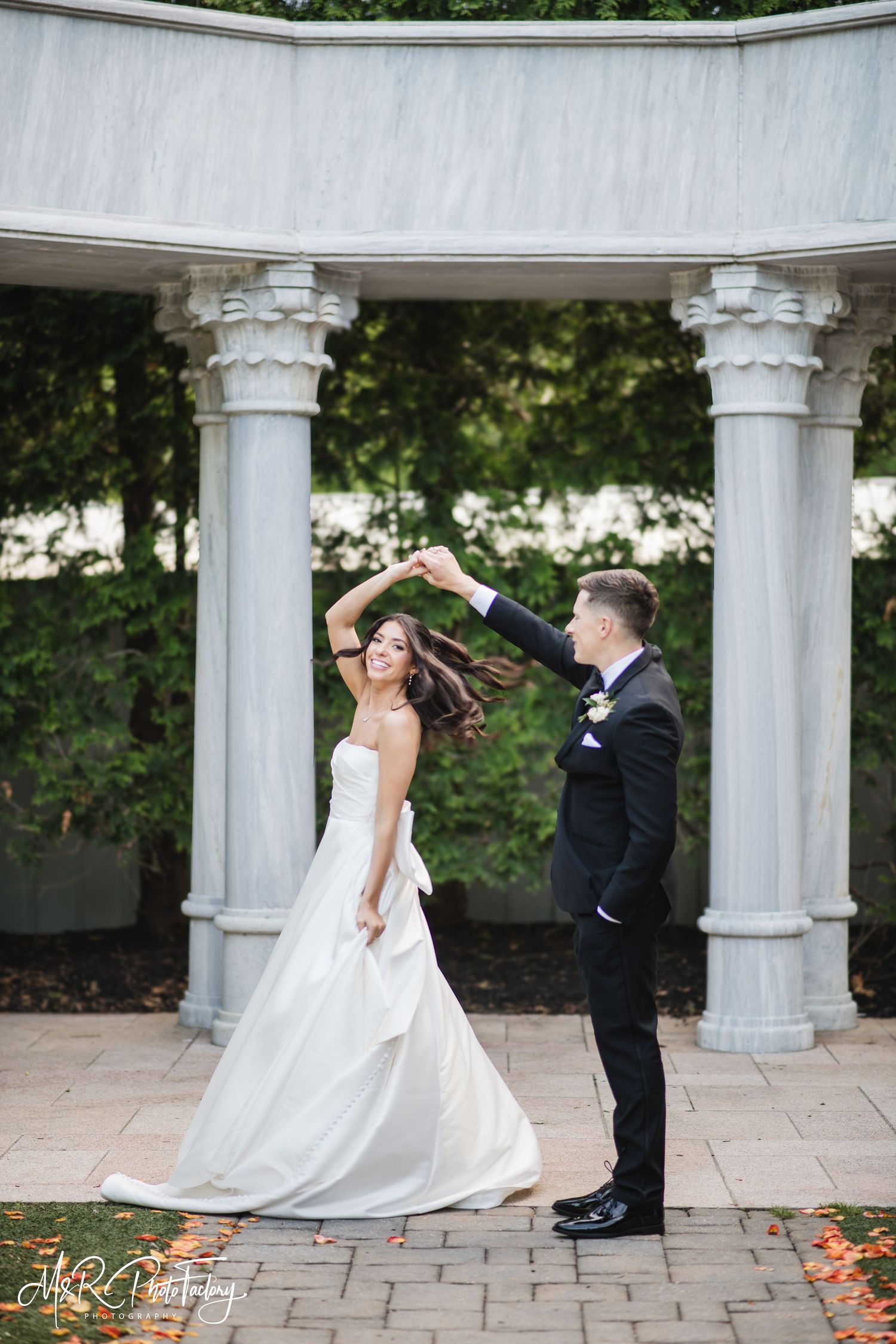 Groom twirls bride in white ball gown under a classic marble columned rotunda on their wedding day.