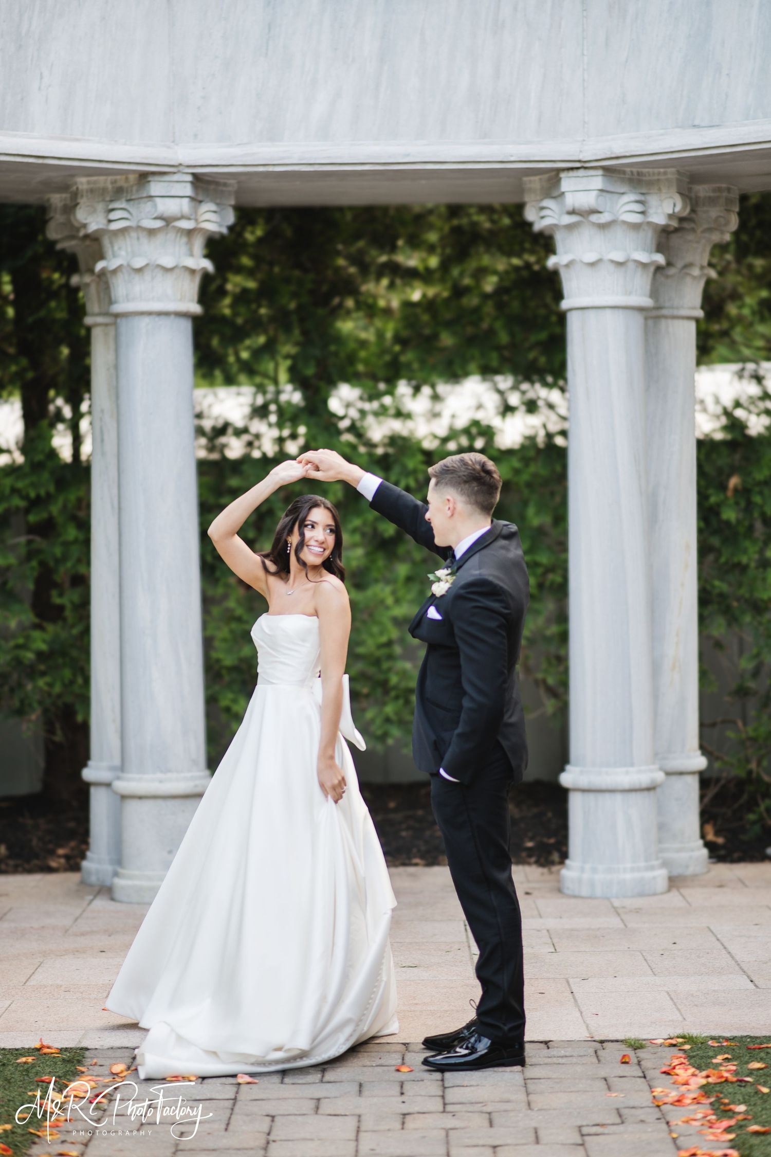 Smiling bride is twirled by her groom under a grand marble rotunda during outdoor wedding portraits.