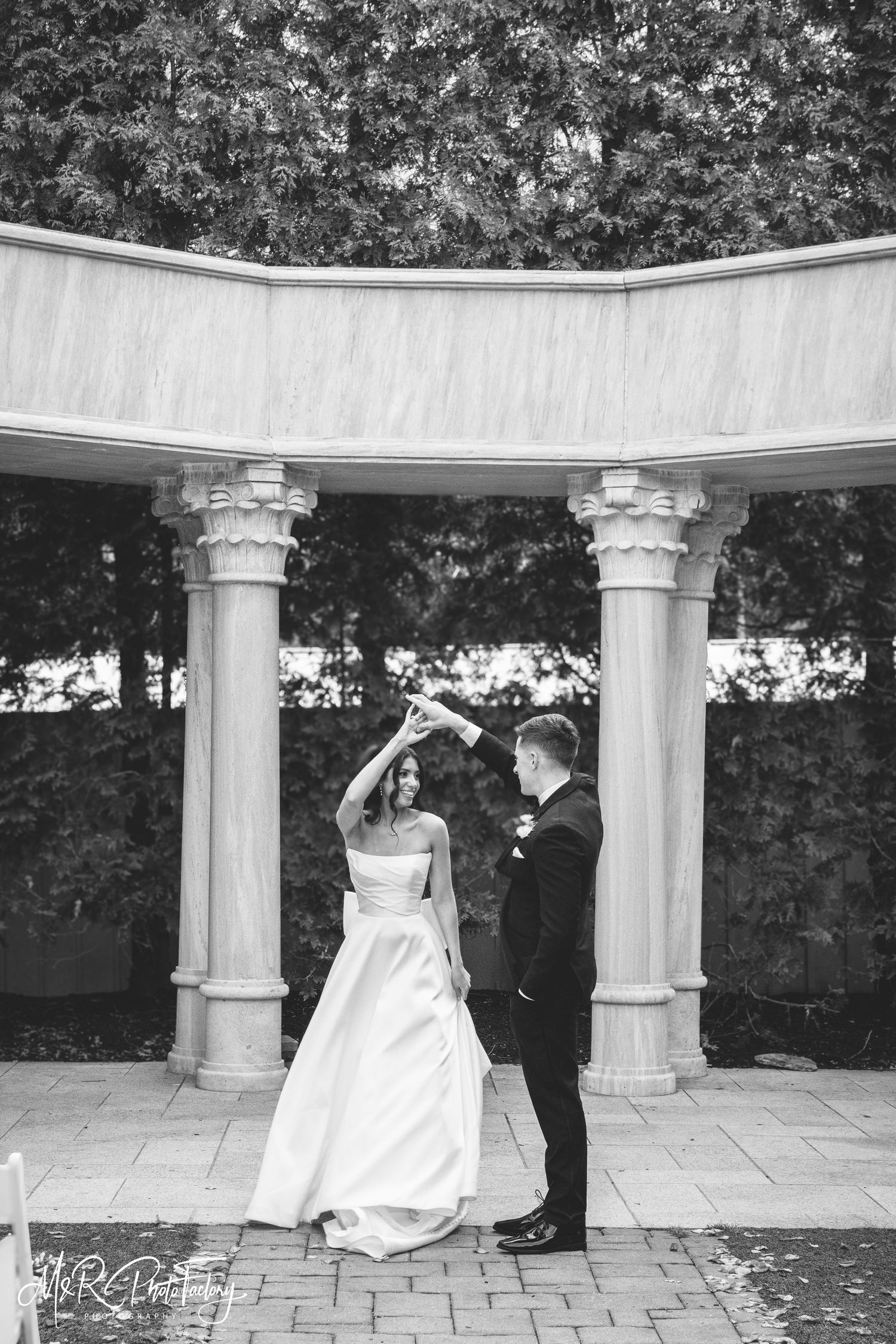 Black and white photo of groom twirling bride under an elegant columned rotunda on their wedding day.