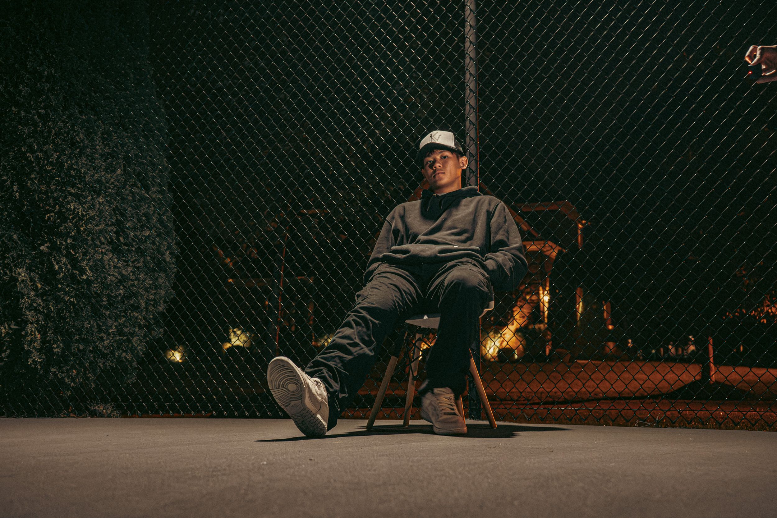 Sequential shots of person relaxing against chain-link fence in dark setting.