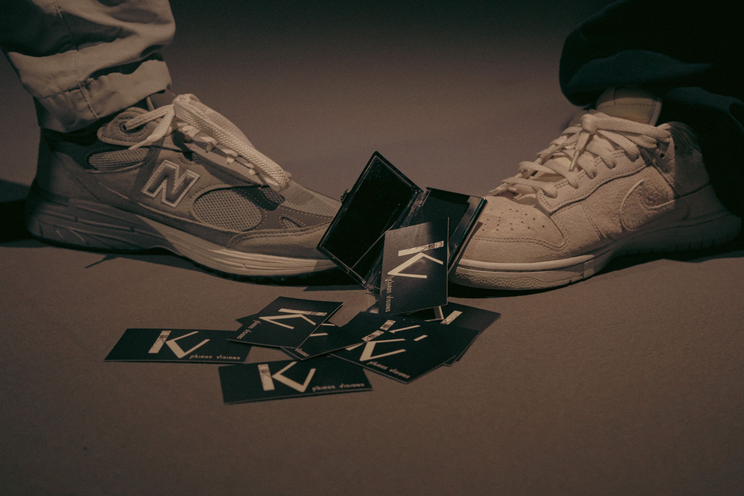 A close-up shot of sneakers and legs resting against a dark background with moody lighting.