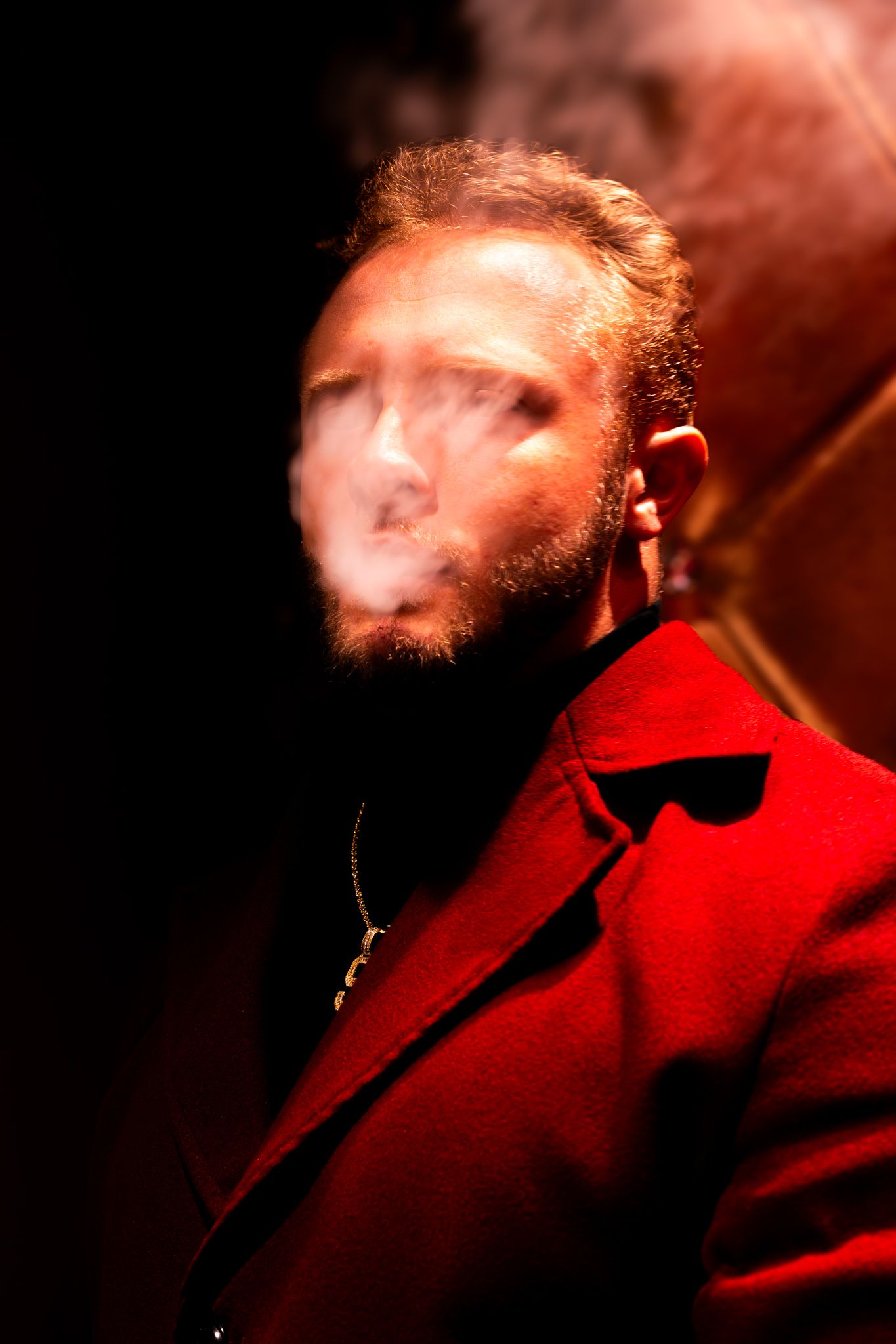 A person in a red jacket exhales smoke creating an atmospheric effect against a dark background.