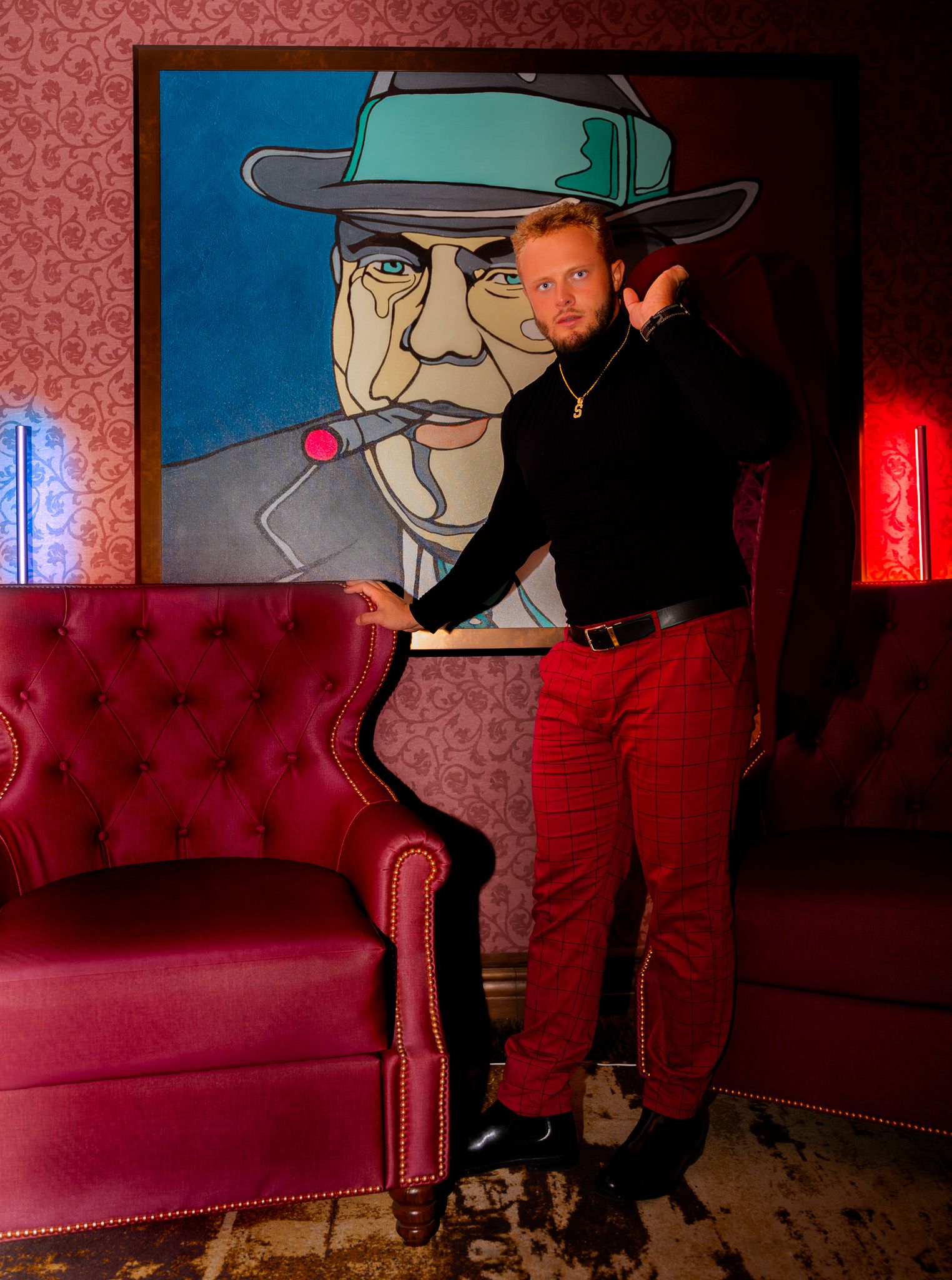 A red velvet couch and wall art create a moody atmosphere in a dimly lit lounge space.