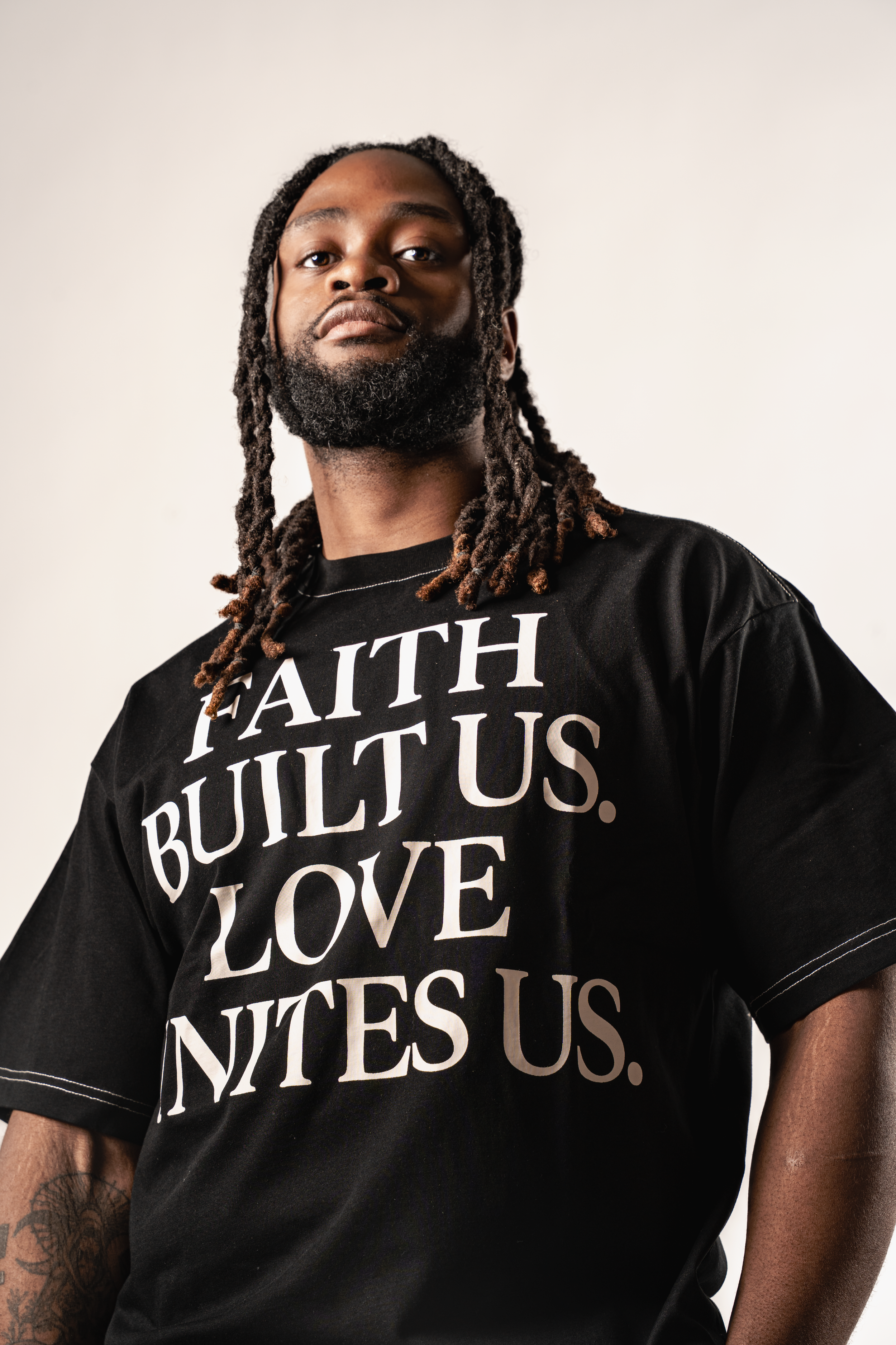A series of black t-shirts with white typography displaying words like 'FAITH' and 'LOVE' against a light background.