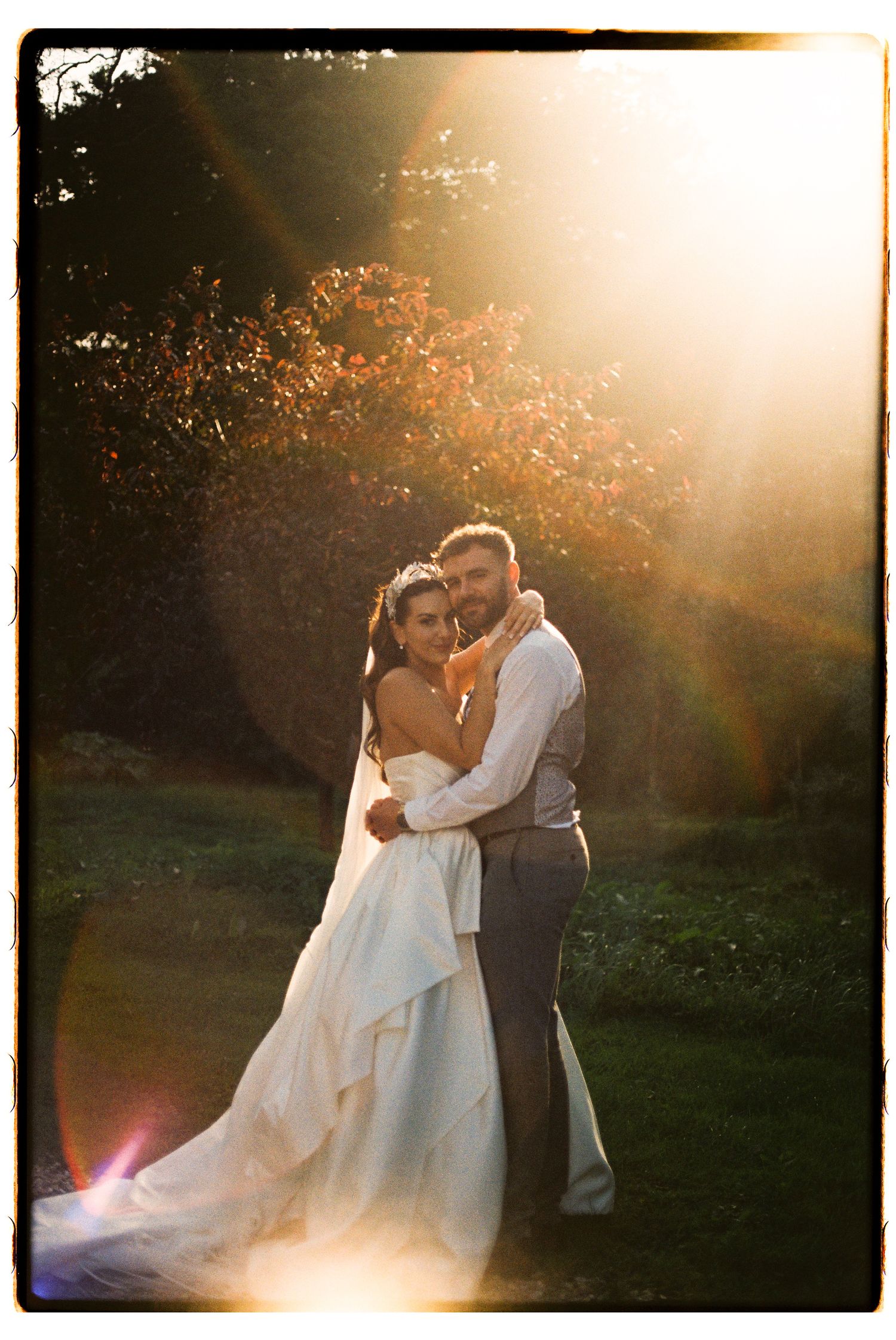 A cheerful wedding party celebrates on the grounds of a historic stone manor house in muted sepia tones.