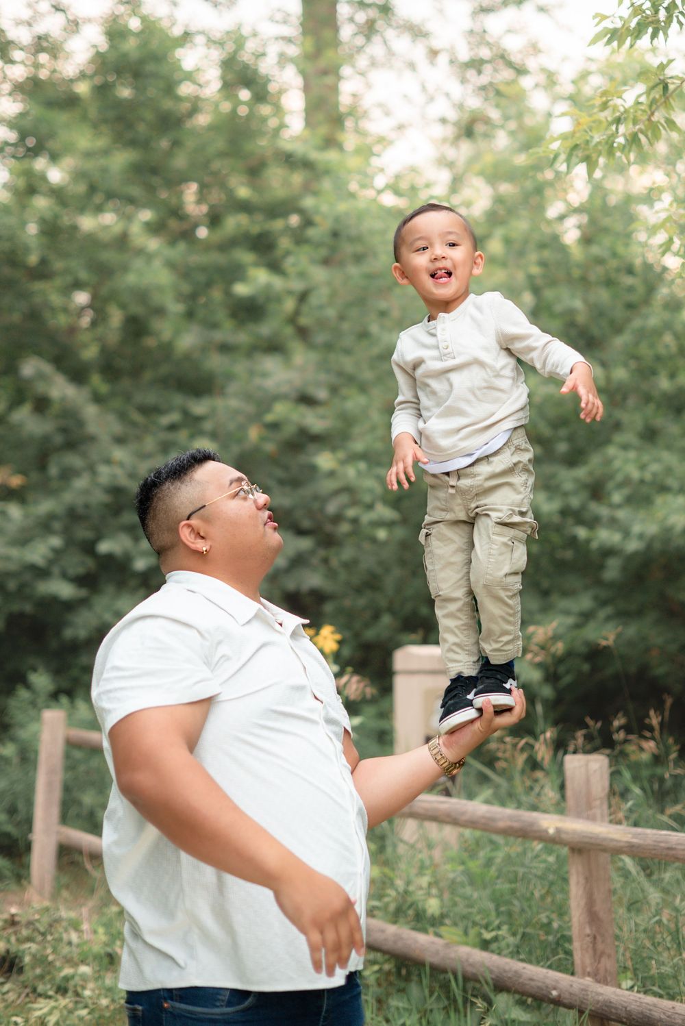 A playful moment in nature as a child balances on someone's hand while standing near a wooden fence in the woods.
