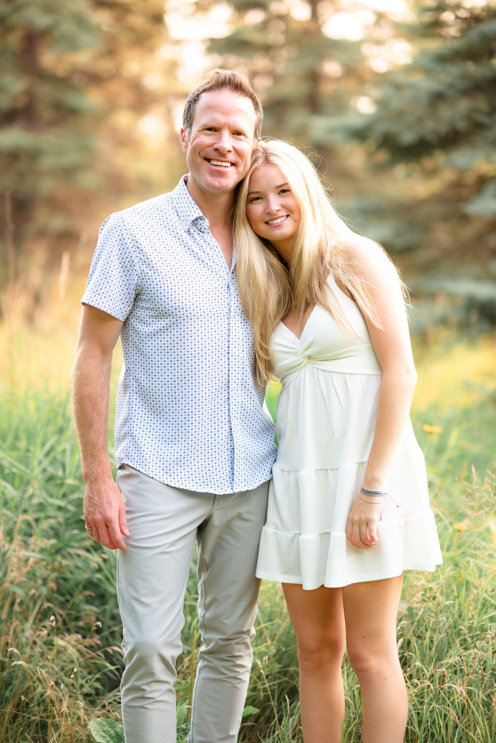 Romantic engagement photo shoot in field during golden hour with couple wearing white summer outfits.