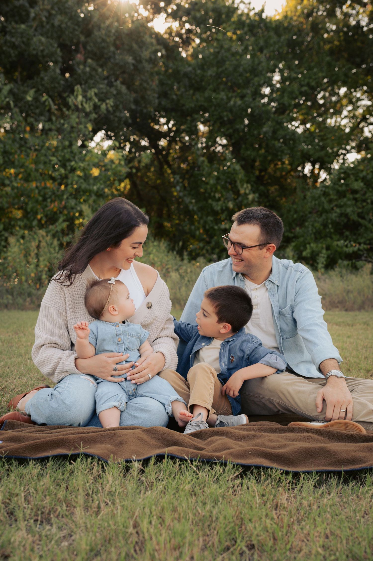 A family sits together on a blanket in a grassy field at sunset during an outdoor photo session.