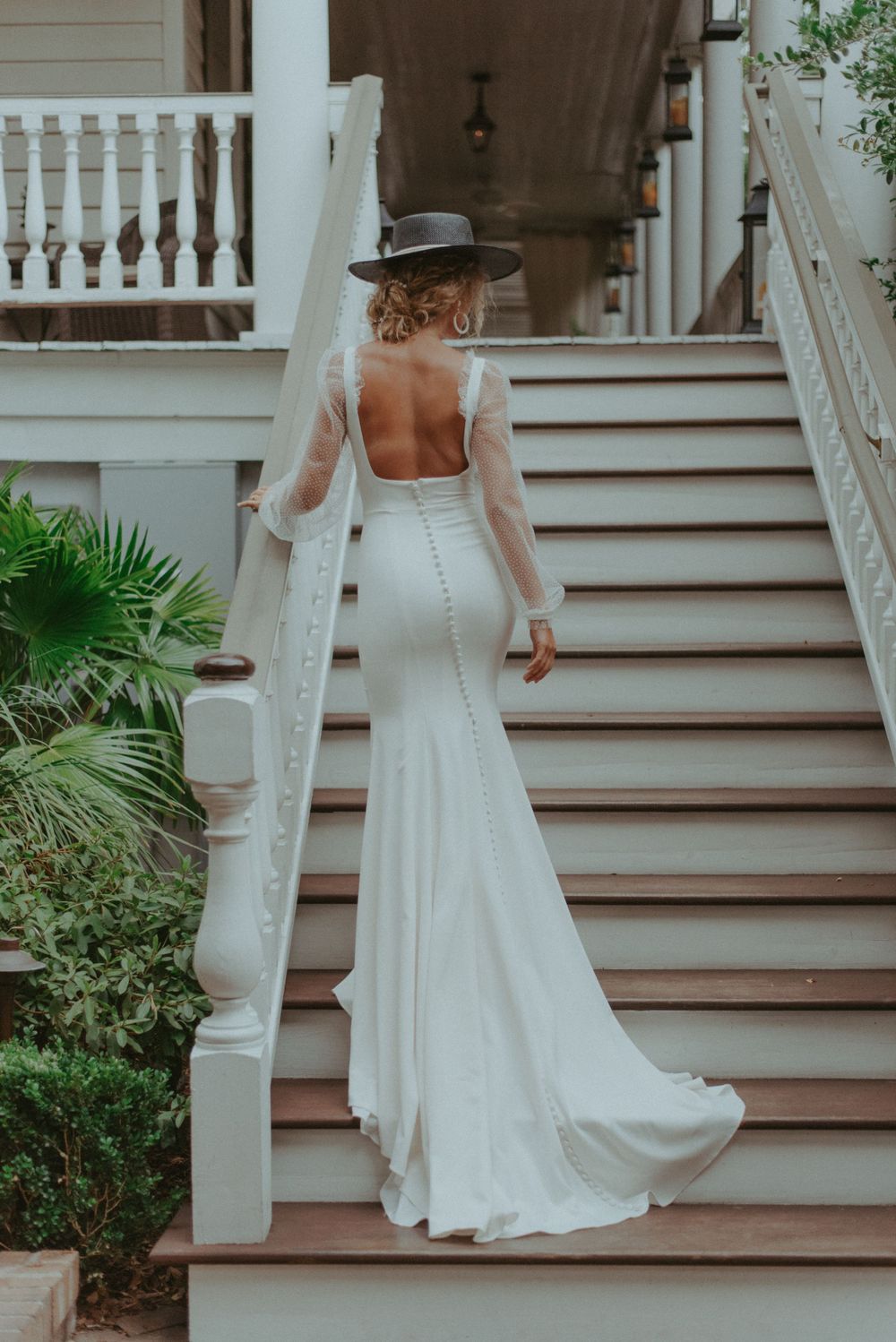 A portrait of a bride walking up stairs with a hat on.