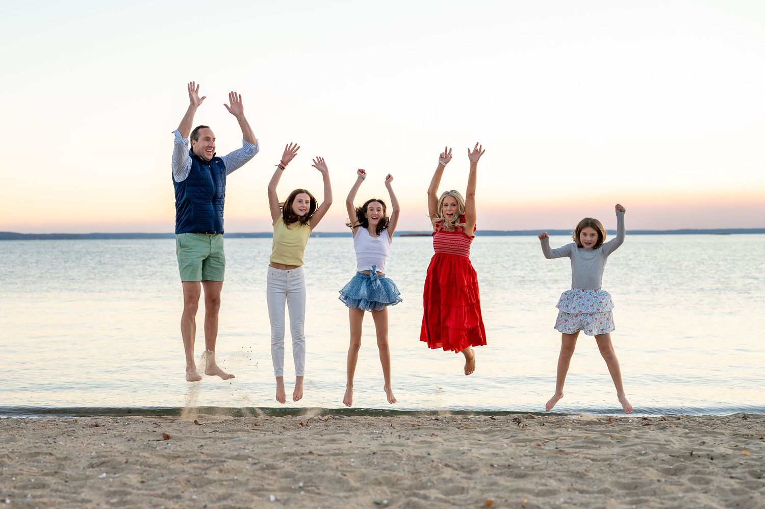People joyfully jumping together on a beach at sunset with calm ocean waters in the background.