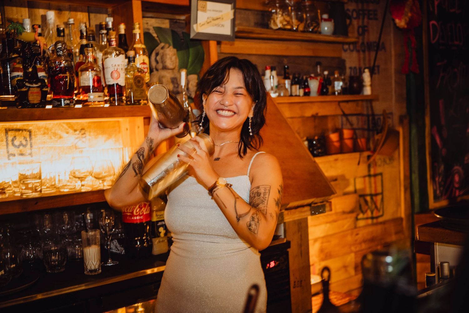 A cozy bar interior with warm lighting and wooden decor features a well-stocked shelf of bottles and spirits.