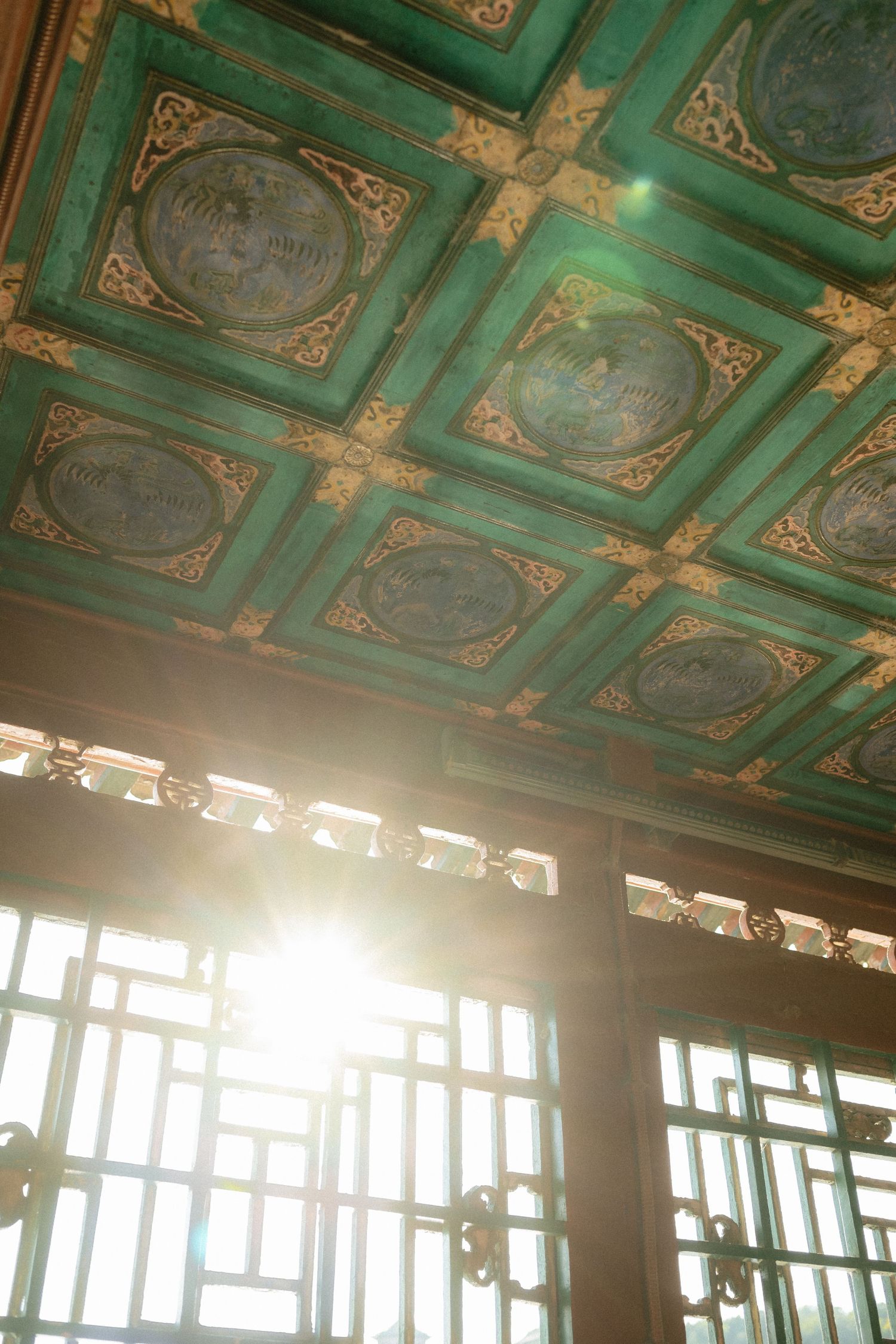 Ornate green and gold coffered ceiling with sunlight streaming through vintage windows in a historic building.
