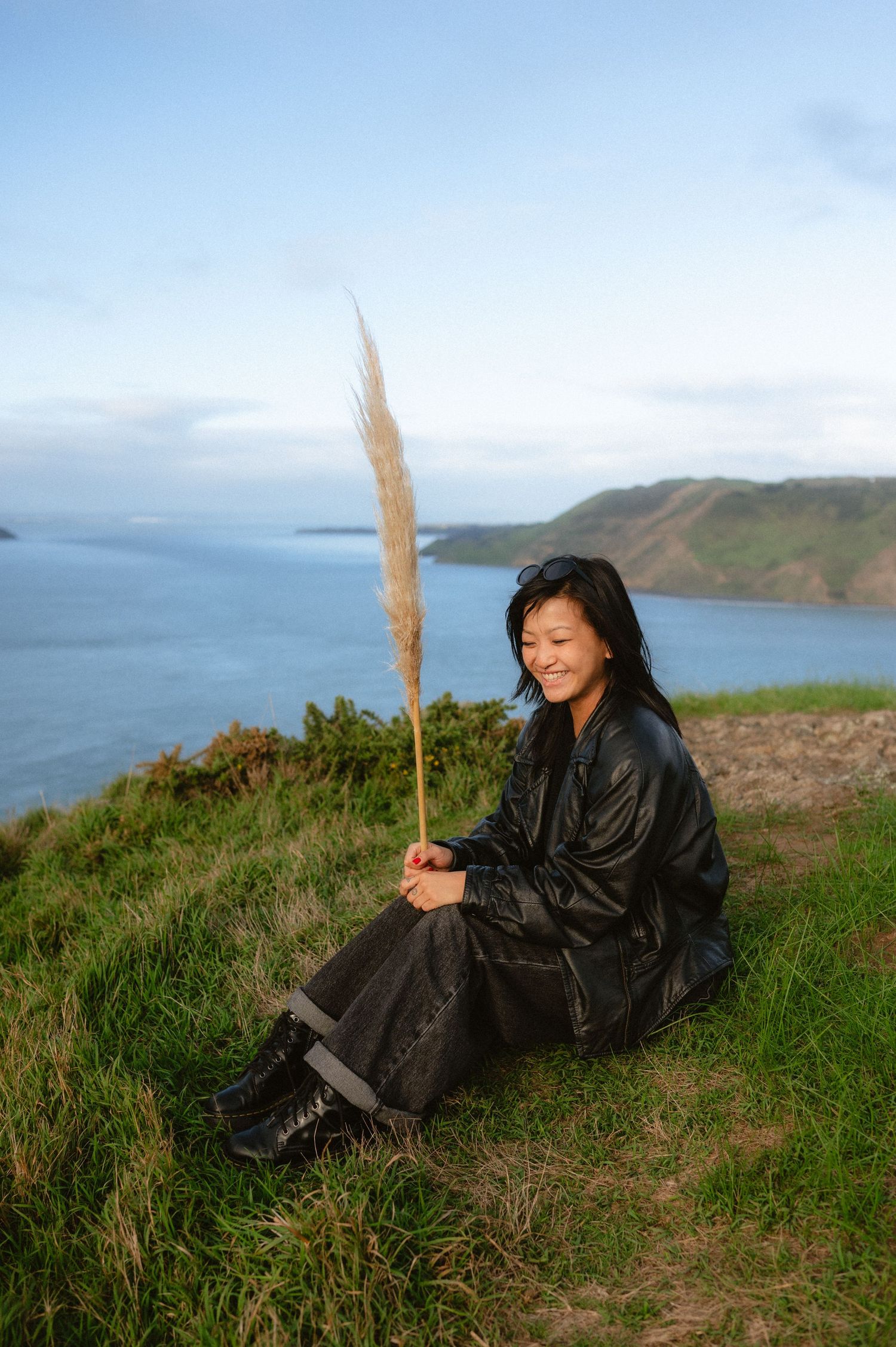 Person in black jacket reclining on coastal hillside overlooking ocean view.