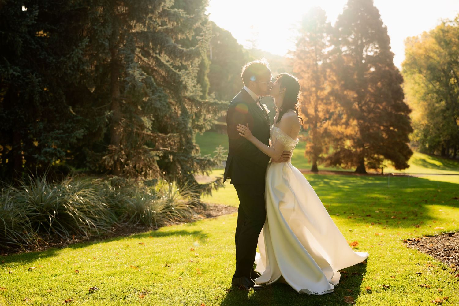 A couple embraces in a sunlit garden setting during a romantic golden hour photoshoot.