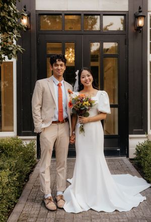 Bride and groom pose holding hands in front of elegant black door with colorful bouquet.