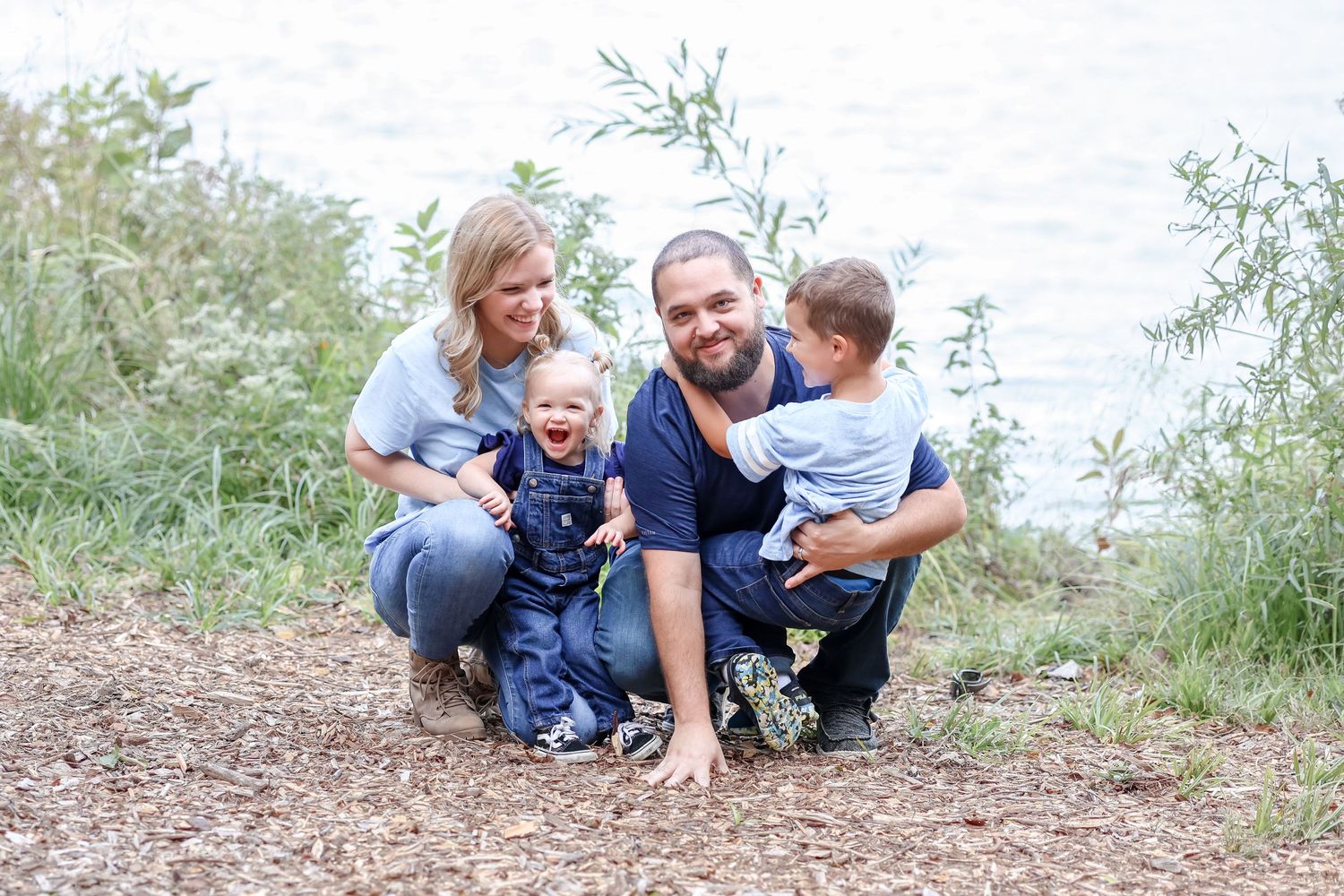 Happy family enjoying time together on a dirt path surrounded by greenery on a sunny day.