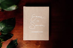 Blush pink wedding album with elegant script text and date on wooden surface.