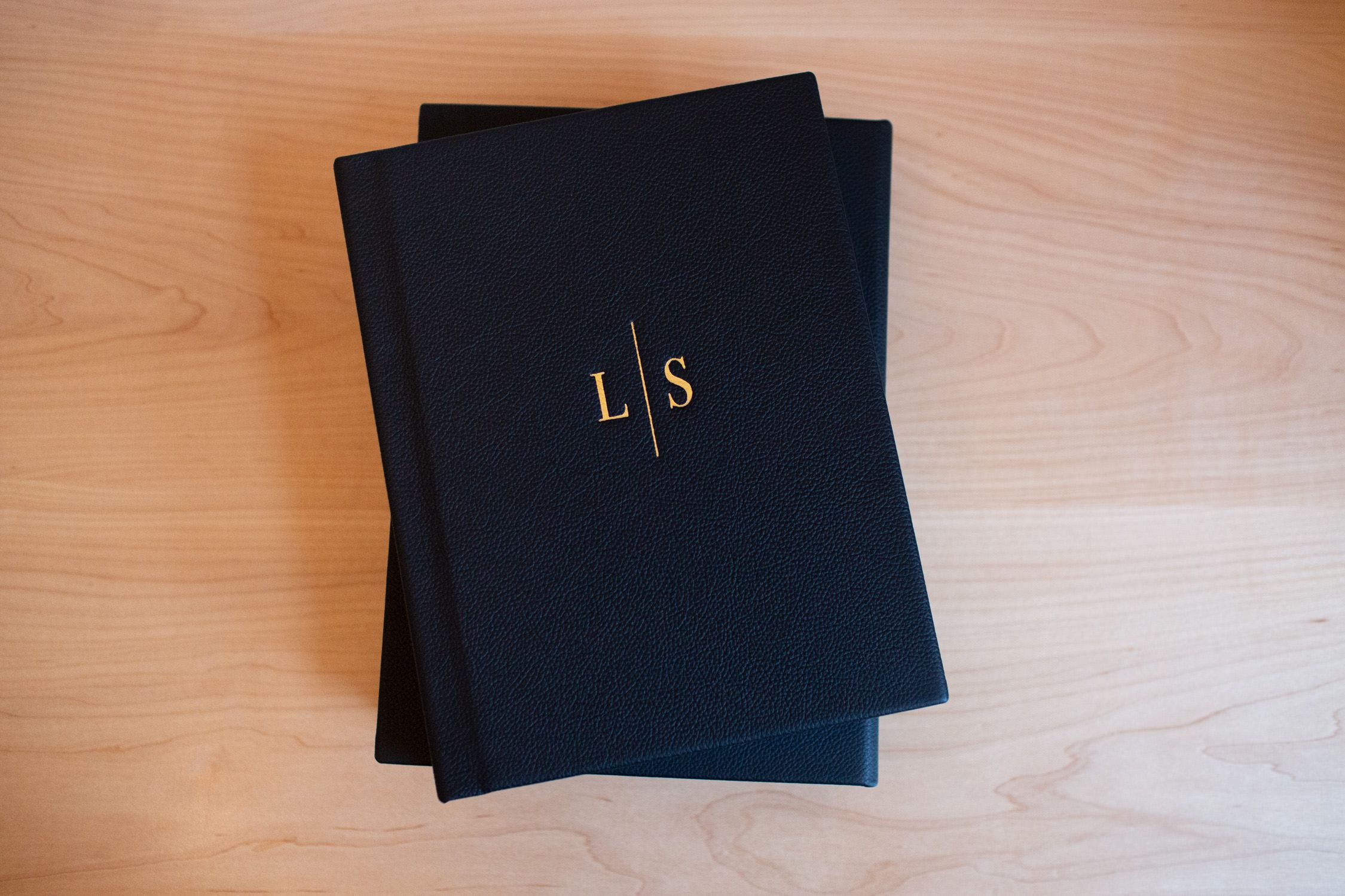 Black hardcover album with elegant gold monogram initials on wooden surface.