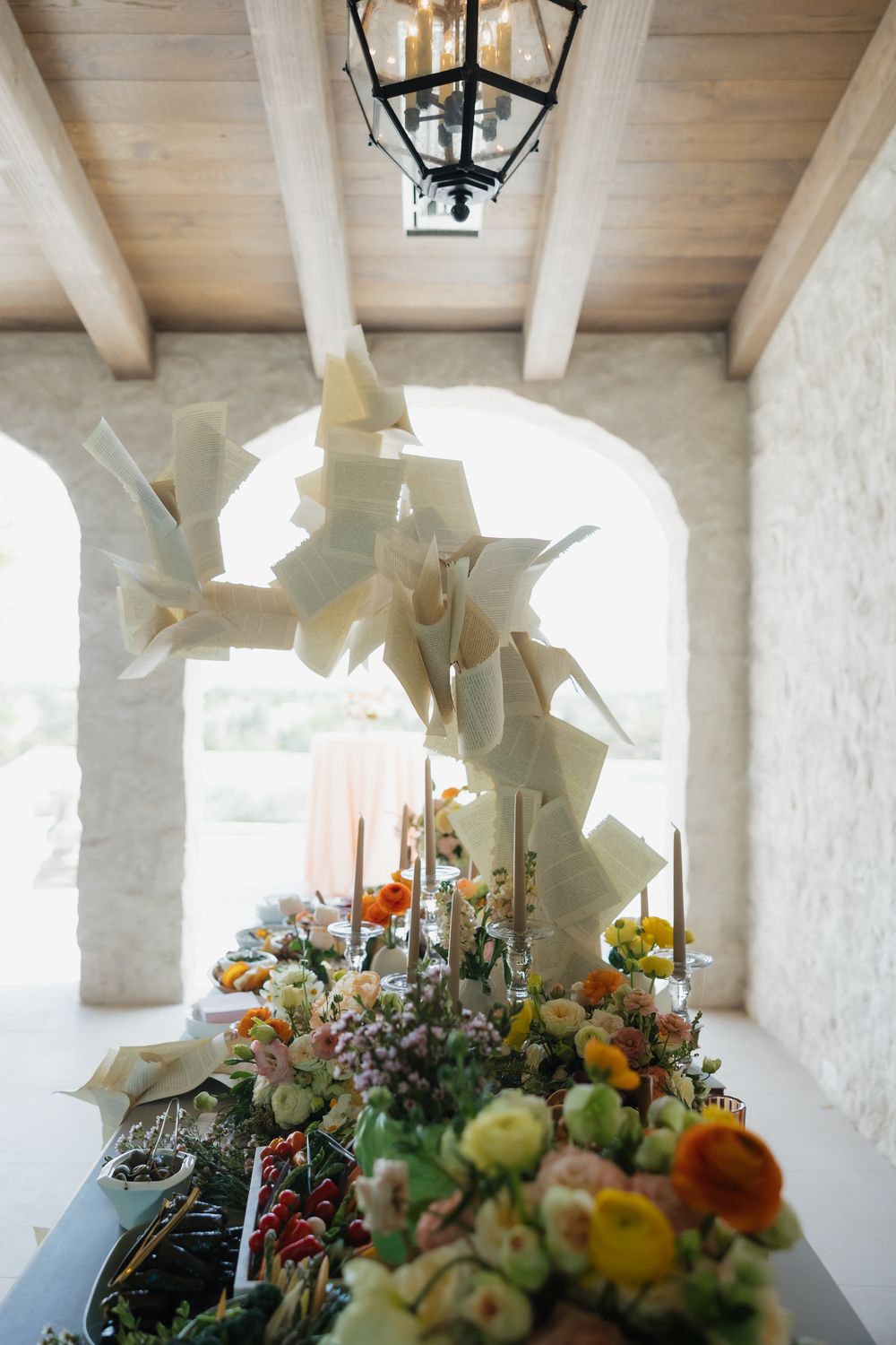White beamed ceiling with hanging lanterns over an elegant floral display featuring yellow and orange blooms.