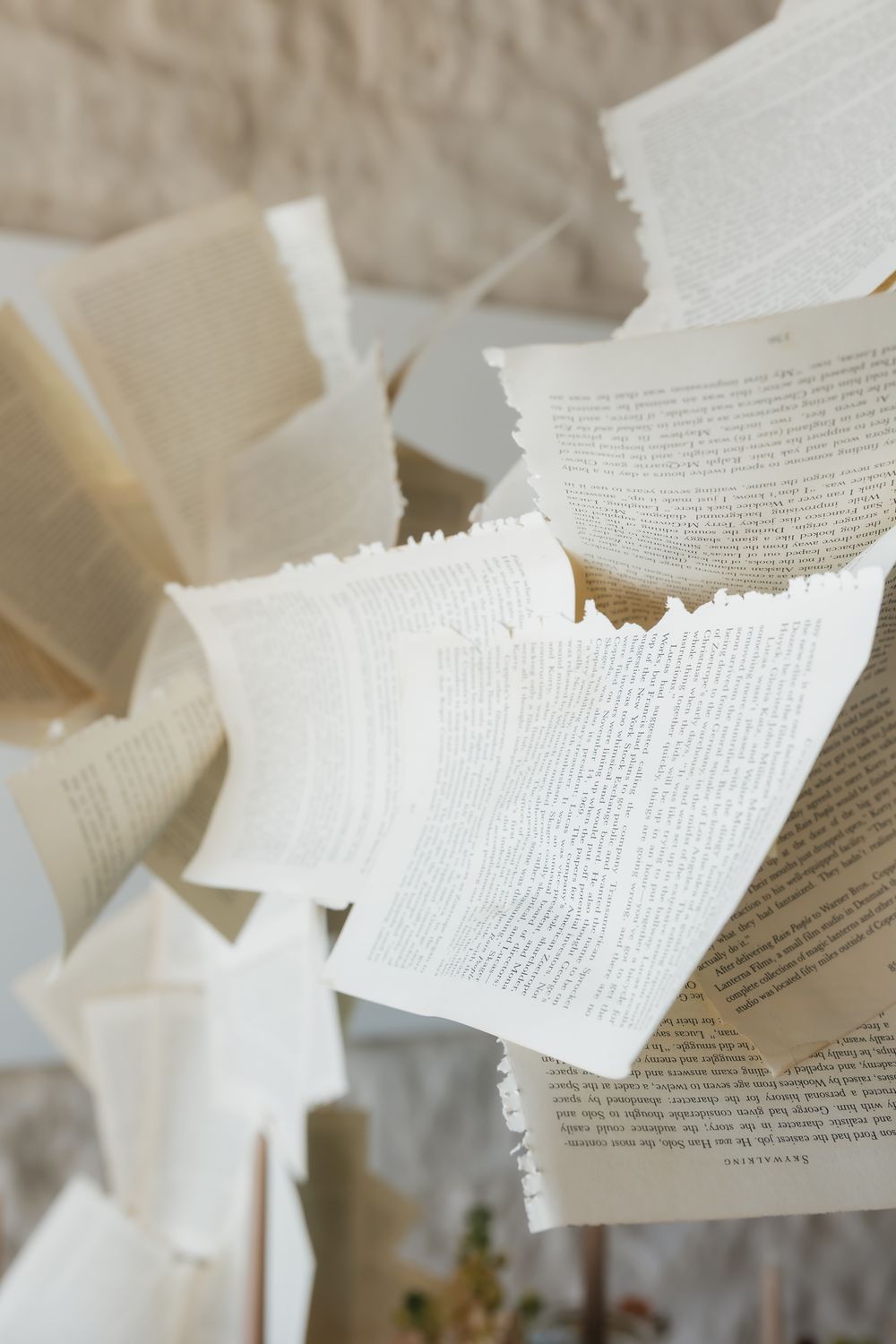 Torn book pages float suspended in air against a light neutral background creating an artistic paper installation.