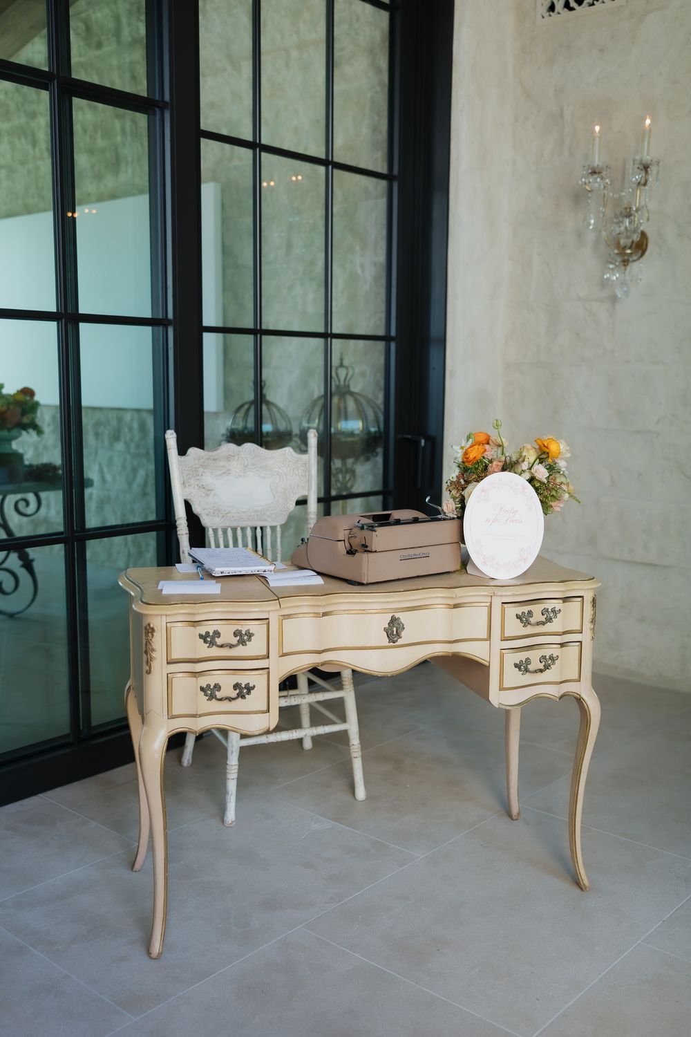 Vintage-style cream colored desk with ornate details displayed in different angles on gray stone flooring.