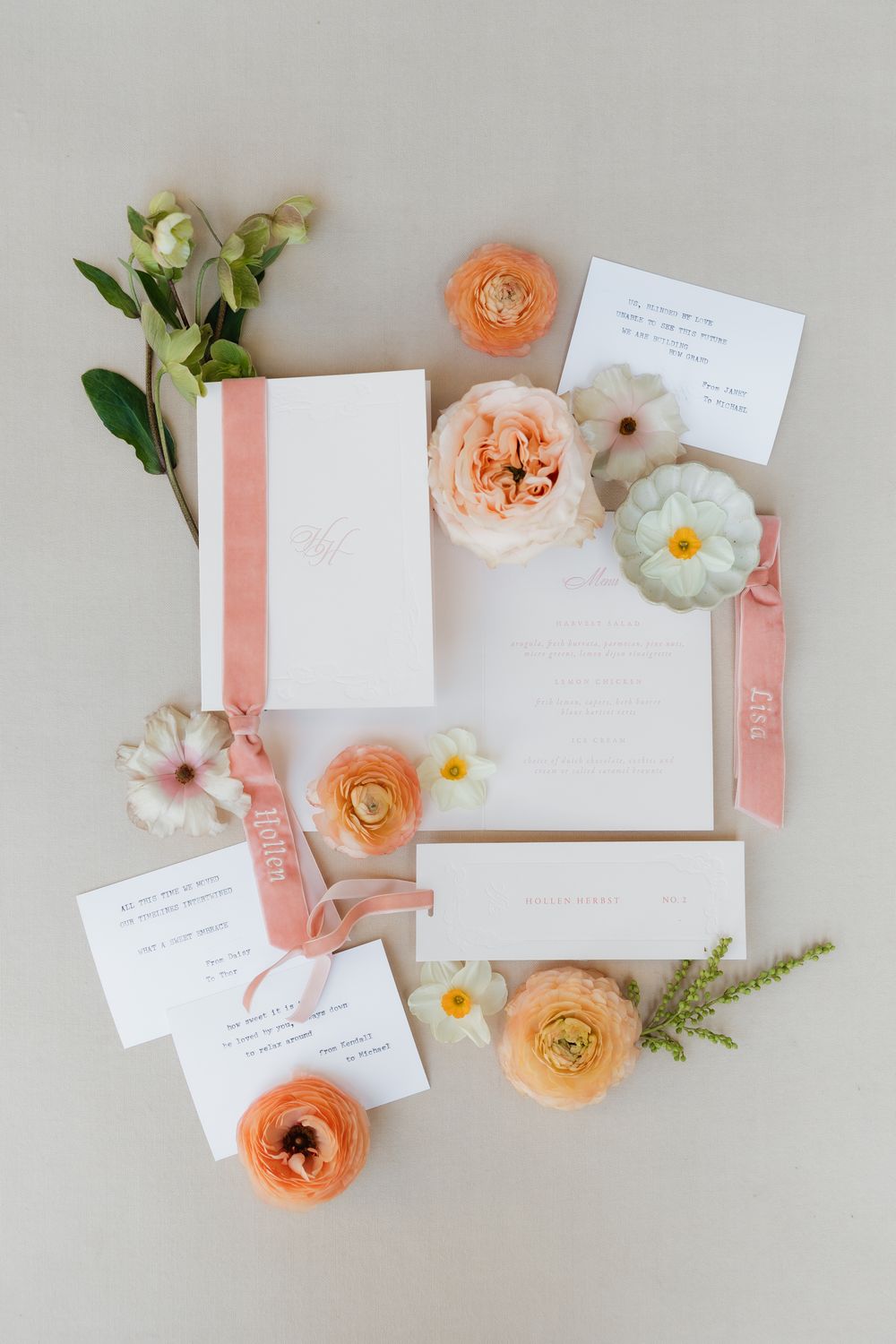 Flat lay of coral and peach ranunculus flowers with white stationery and greenery on light gray background.