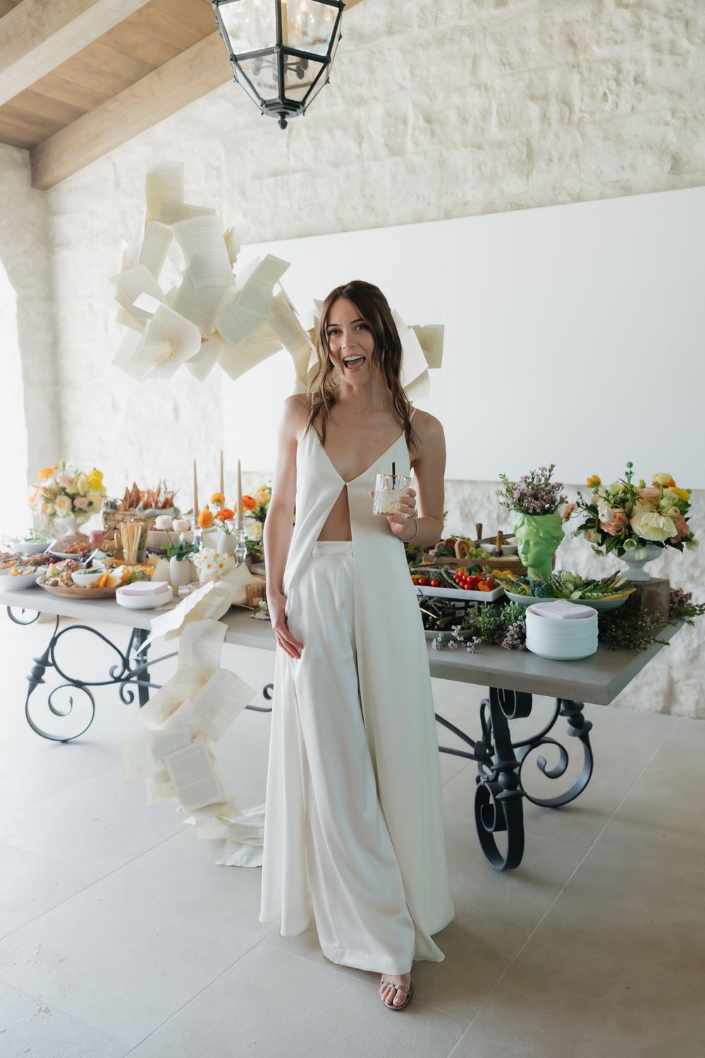 Elegant wedding reception setup with white tables, lanterns and floral centerpieces in a covered stone patio.