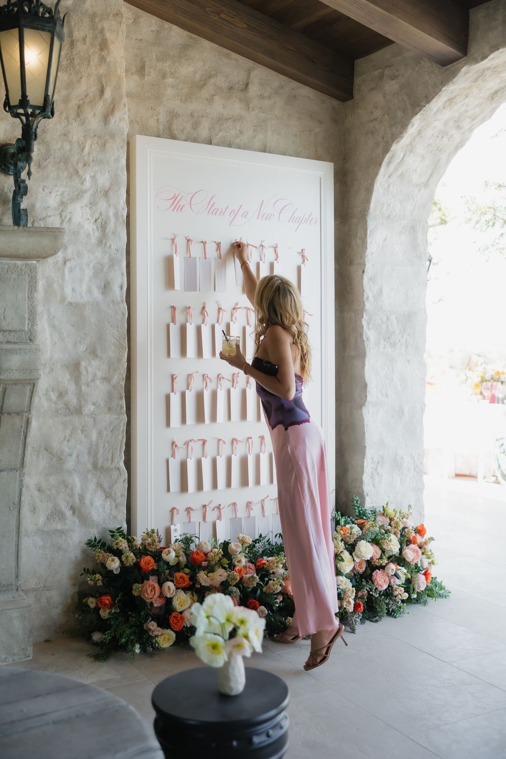 Wedding seating chart display with floral arrangements and lantern in Mediterranean-style archway.