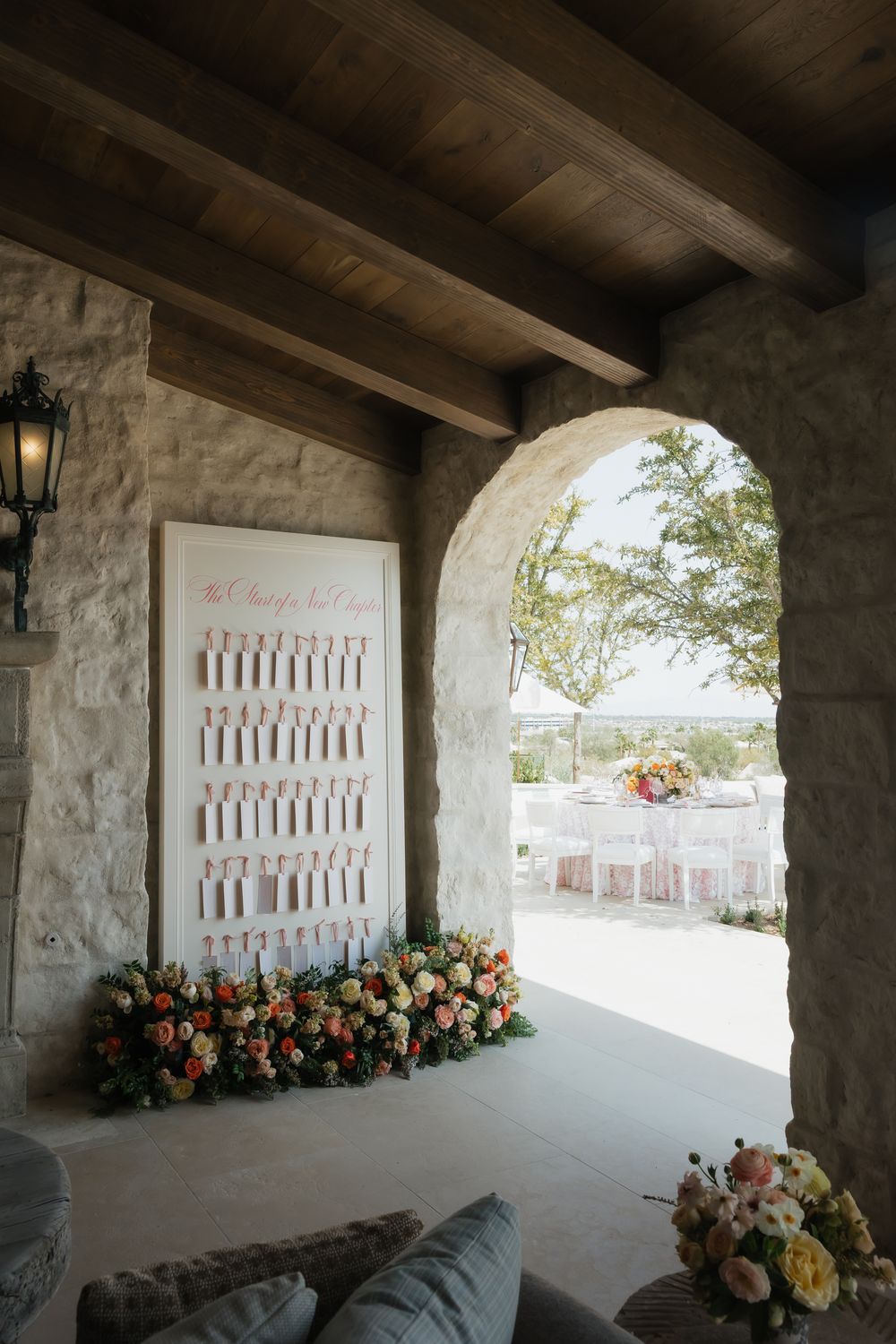 Rustic covered patio with stone walls features a decorative white lattice panel and colorful floral arrangements.