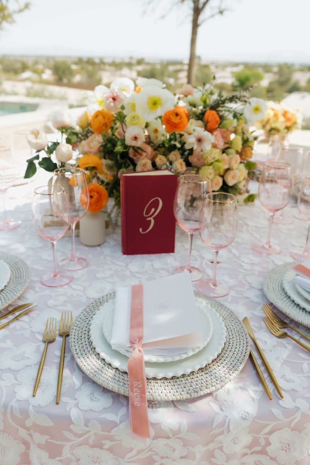 Elegant wedding table settings with pink and white floral centerpieces, silver charger plates, and burgundy table numbers.