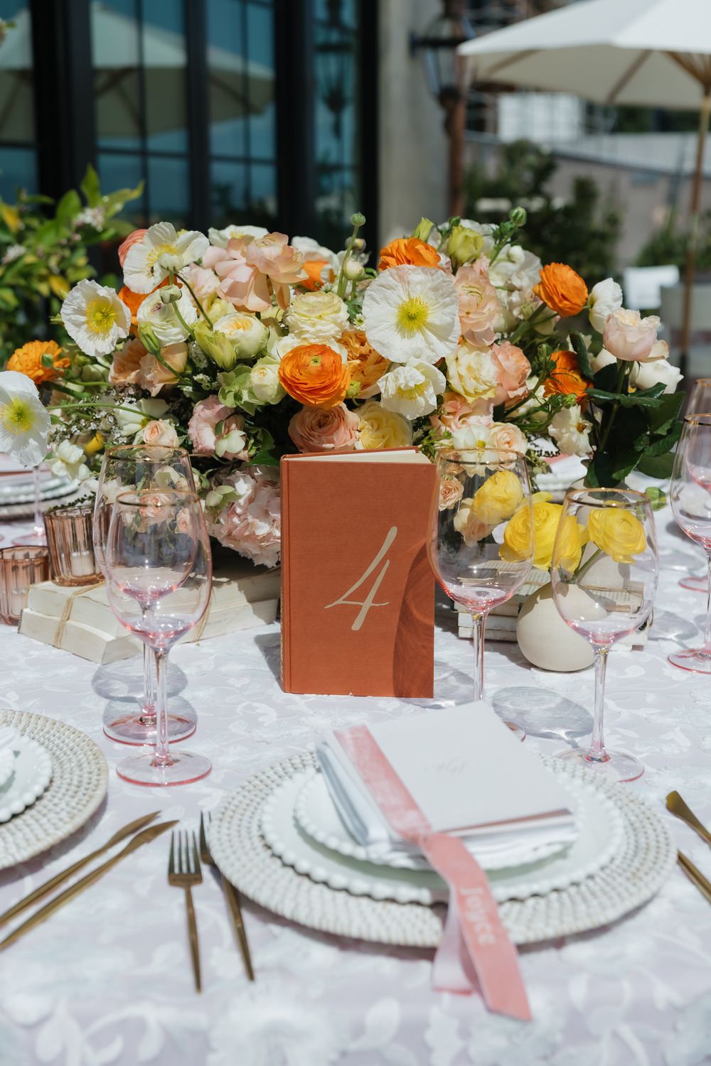 Elegant table settings with pink and orange floral centerpieces in copper boxes at a formal event.