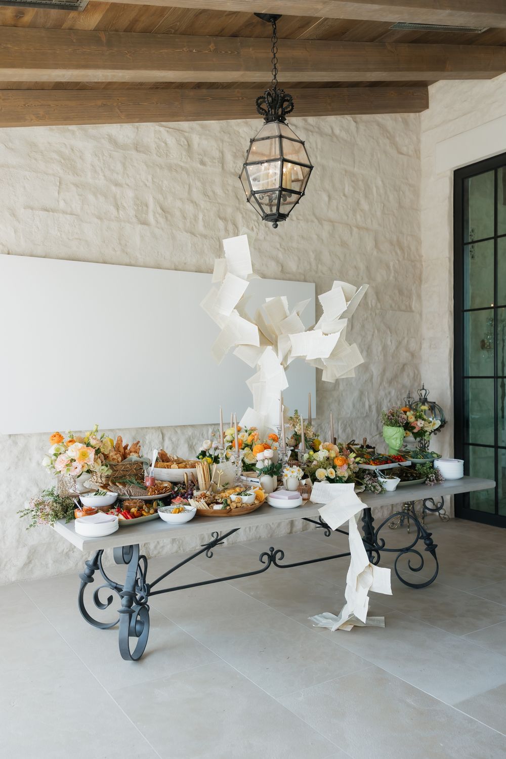 Rustic covered patio with wrought iron sconces and a decorative wheelbarrow filled with colorful floral arrangements.
